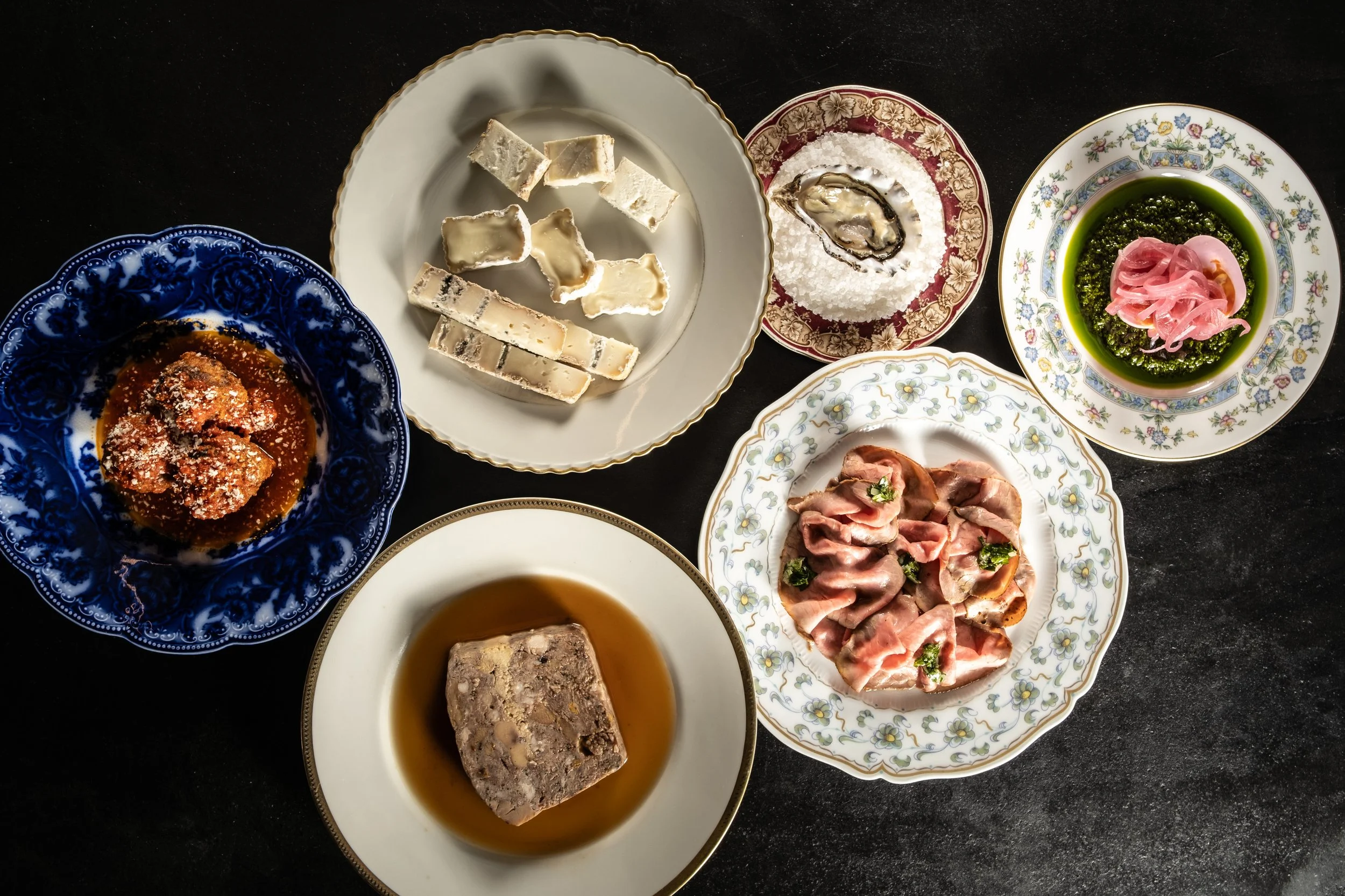 Varia selezione di antipasti e salumi italiani serviti in piatti decorati su un tavolo nero.
