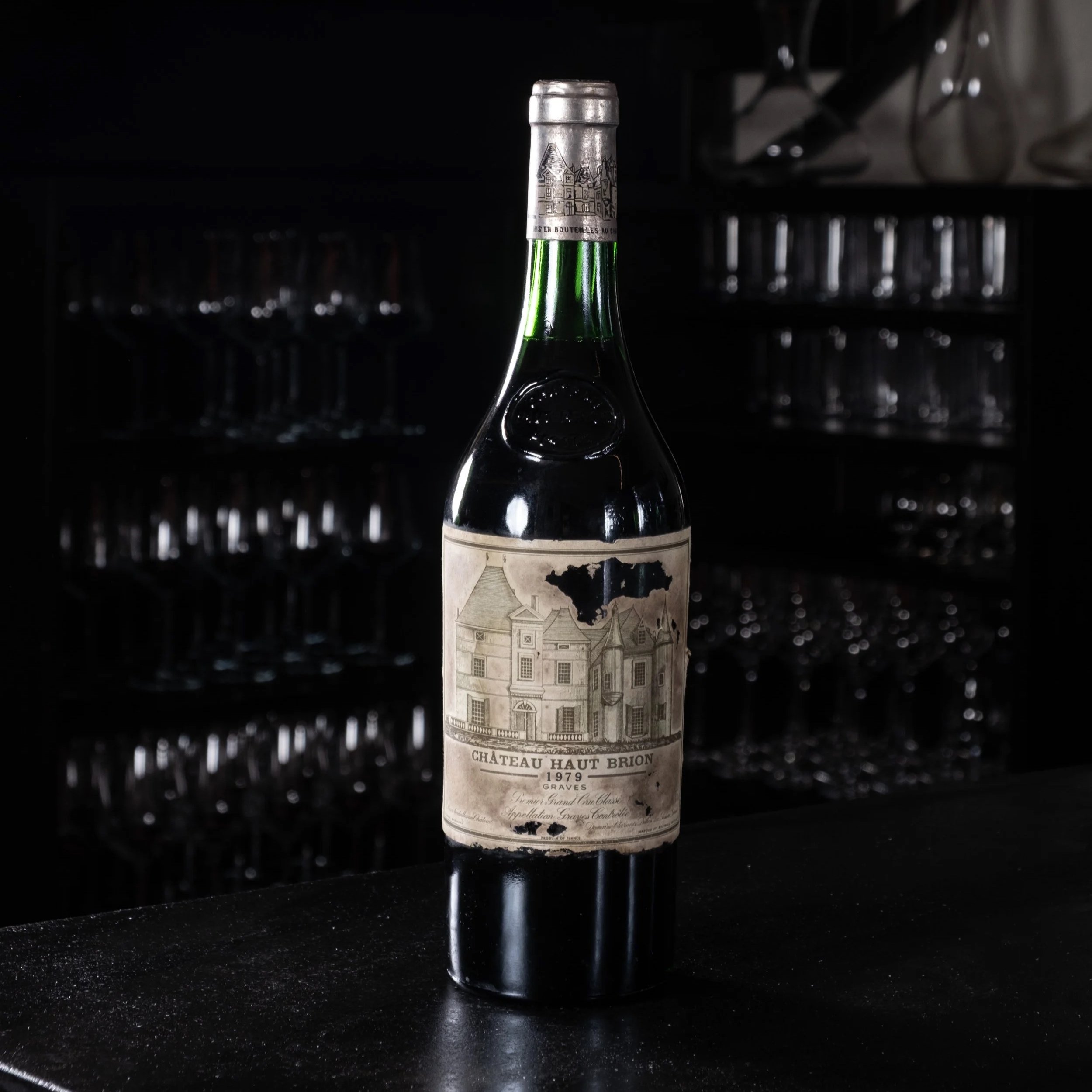 Bottiglia di vino rotta con etichetta datata 1979, Chateau Haut Brion, in un ambiente scuro.