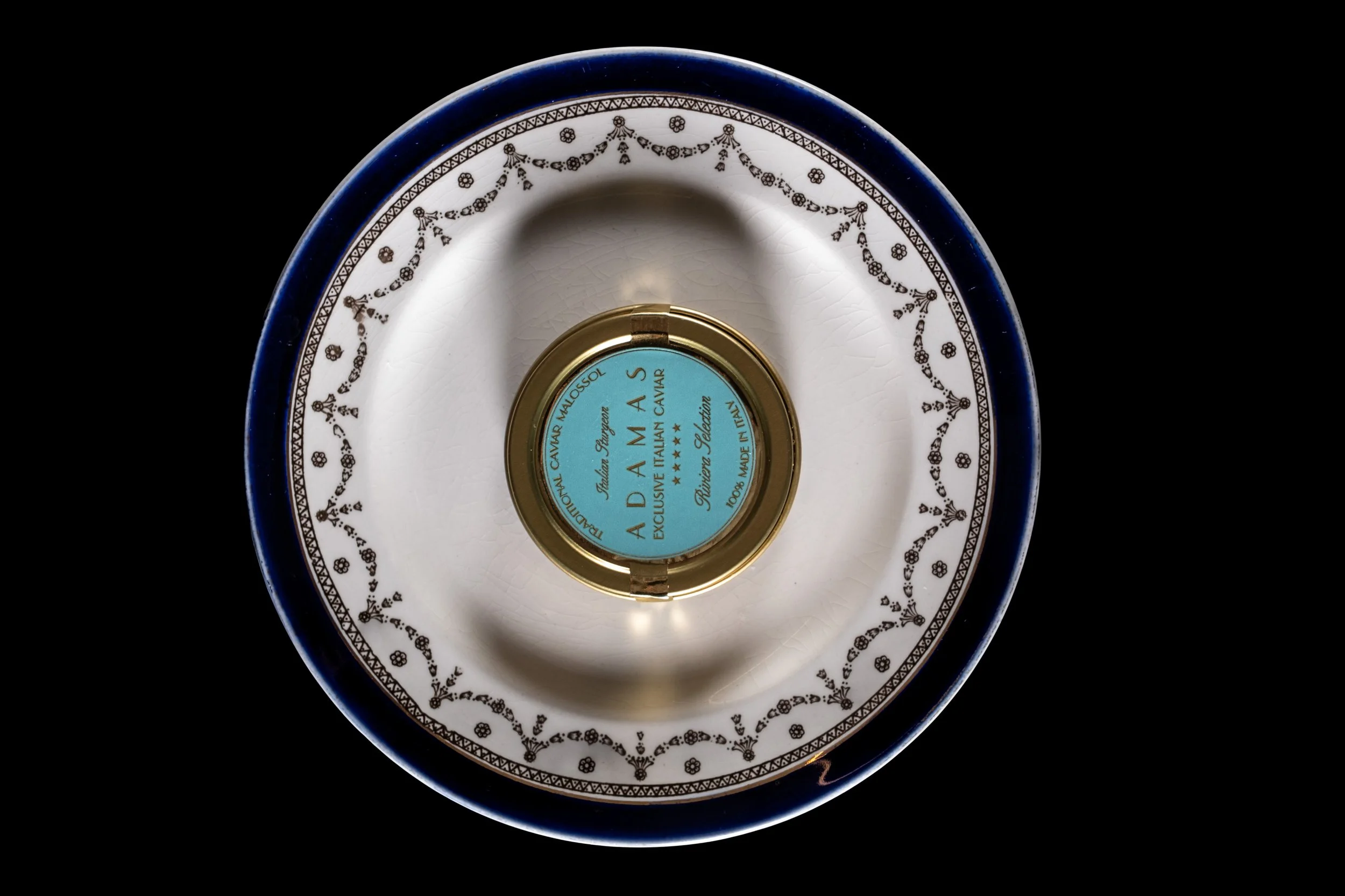 Table en céramique blanche décorée de motifs noirs et d'une bordure bleue, avec une boîte de caviar placée au centre