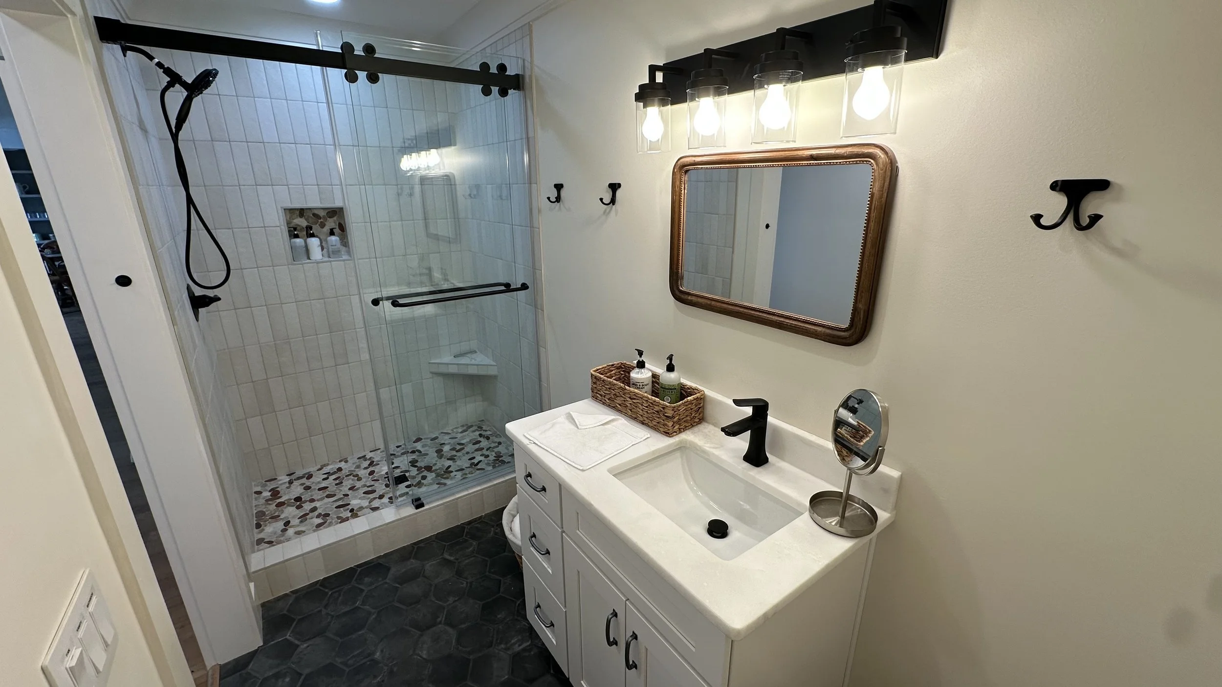 Bathroom with a glass-enclosed shower area, white vanity with a black faucet, oval mirror, and decorative lighting above the mirror
