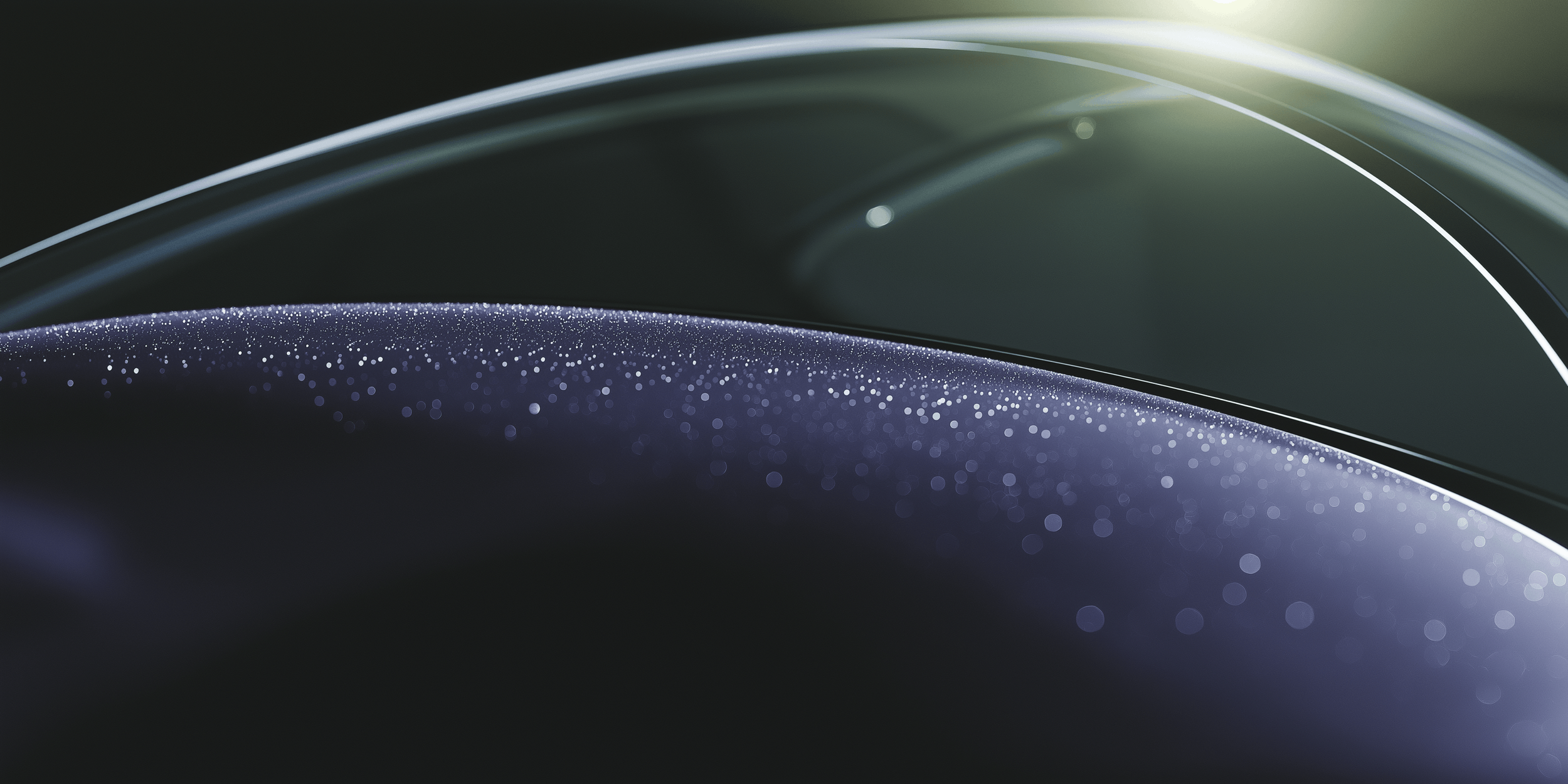 Close up of curved glass surfaces with reflections and small droplets or dust particles, included on the By Goldenburg site to emphasize clarity and meticulous detailing.