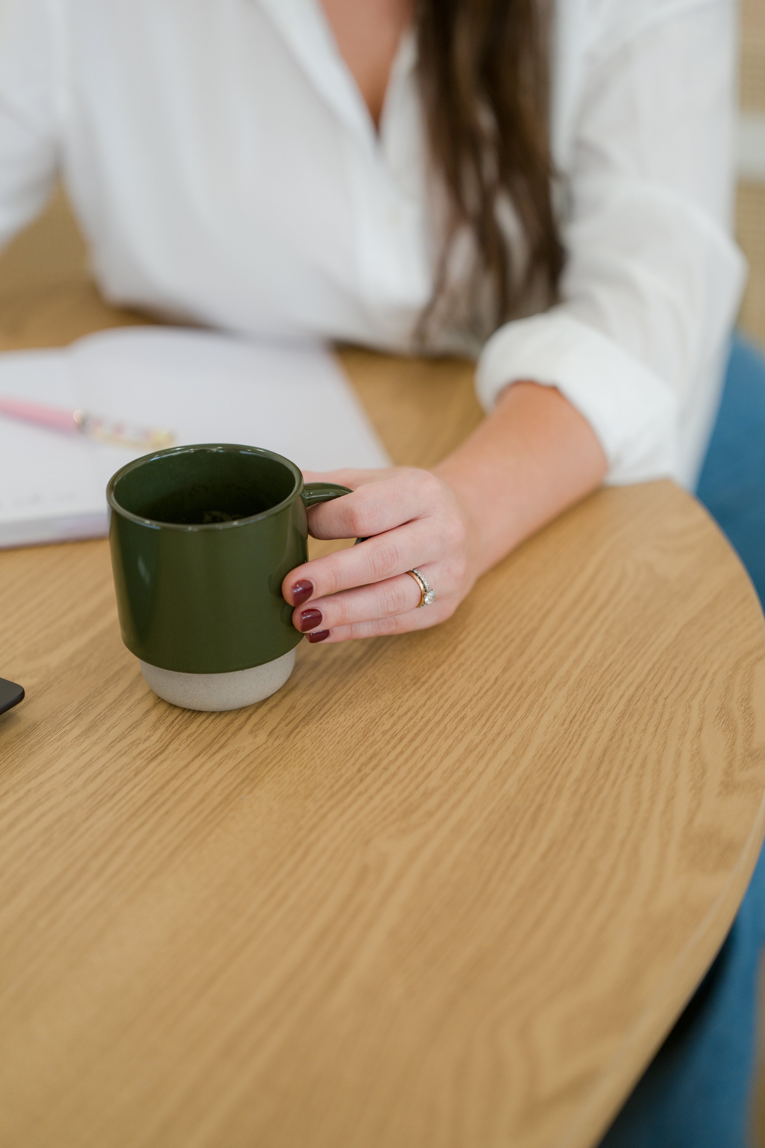 A person's arm resting on a wooden railing, wearing a silver watch and a white long sleeve shirt with black nail polish.