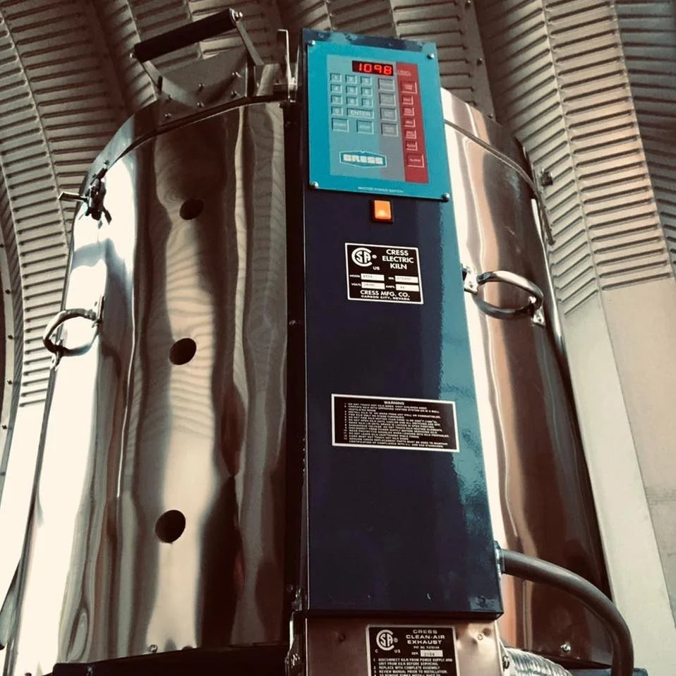 A large industrial electric kiln with digital control panel, situated indoors with corrugated metal walls.