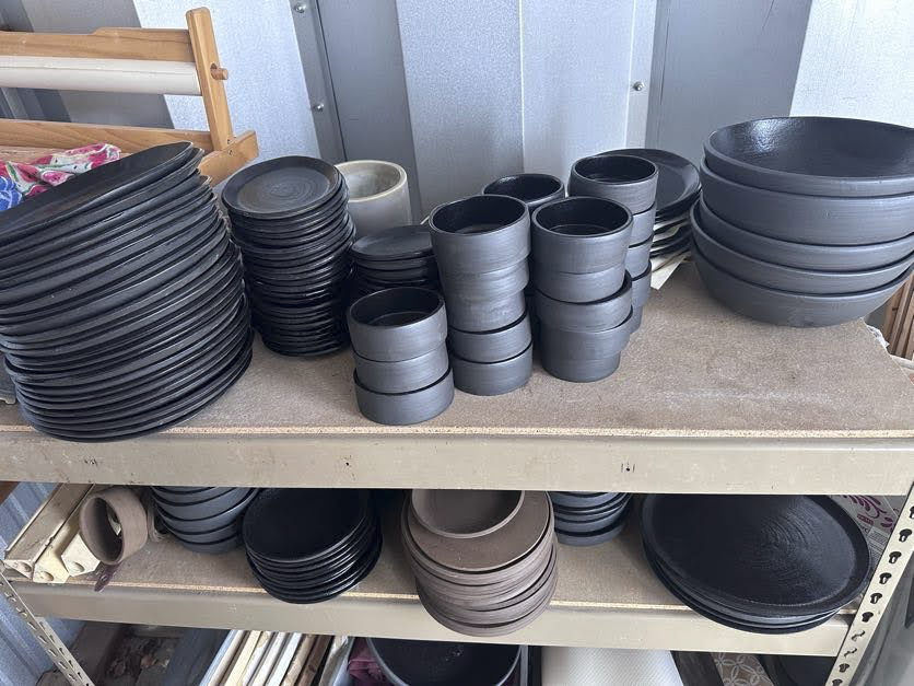 Stacks of black and gray ceramic bowls and plates on metal shelving