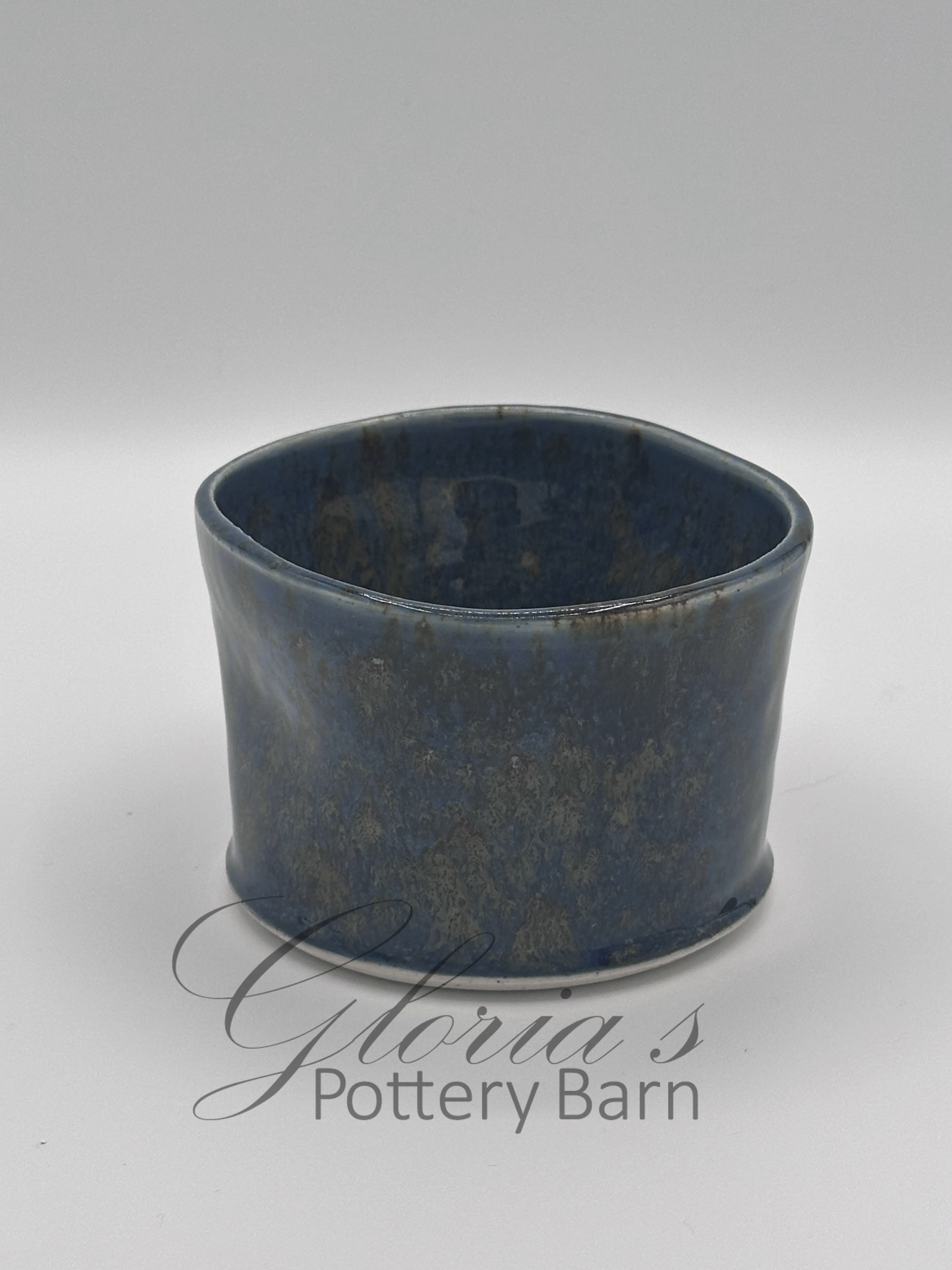 A blue glazed ceramic bowl with a textured finish placed on a white surface with the text 'Gloria's Pottery Barn' underneath.