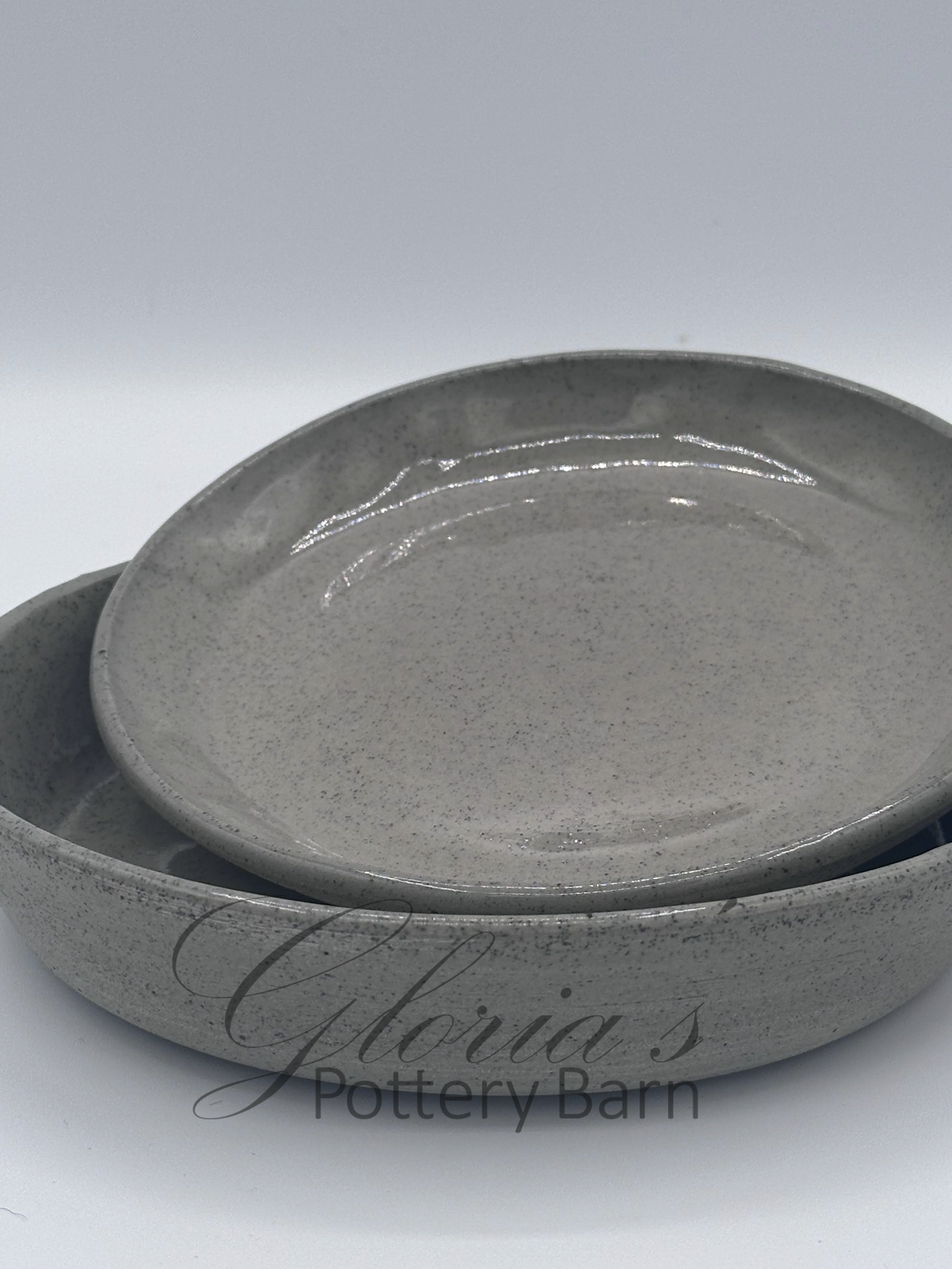 Two stacked ceramic bowls with a speckled gray glaze, with the top bowl slightly smaller, set against a plain background.