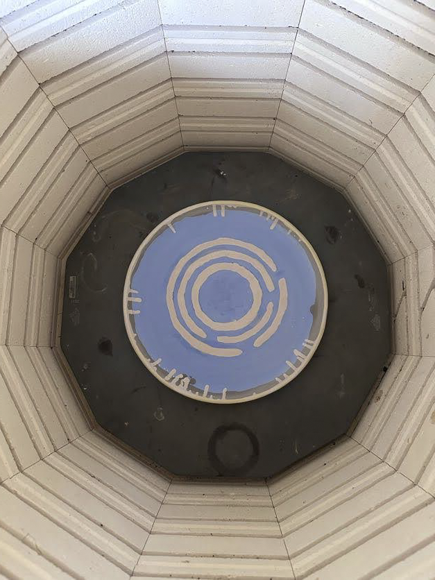 Roof with a circular skylight in the center, featuring a labyrinth design painted in blue and white.