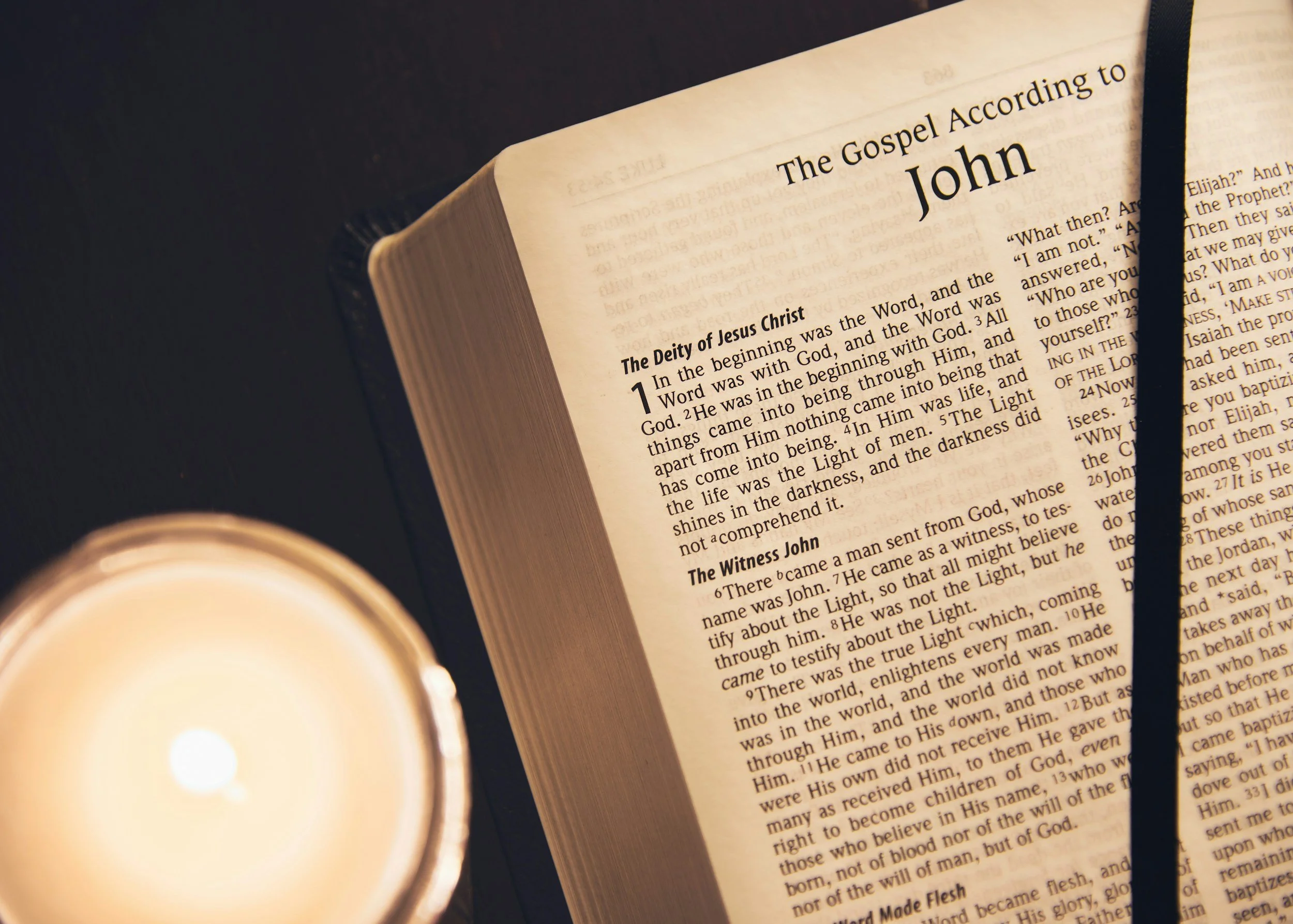 Open Bible page showing the beginning of the Gospel of John with a candle in front of it, casting light.