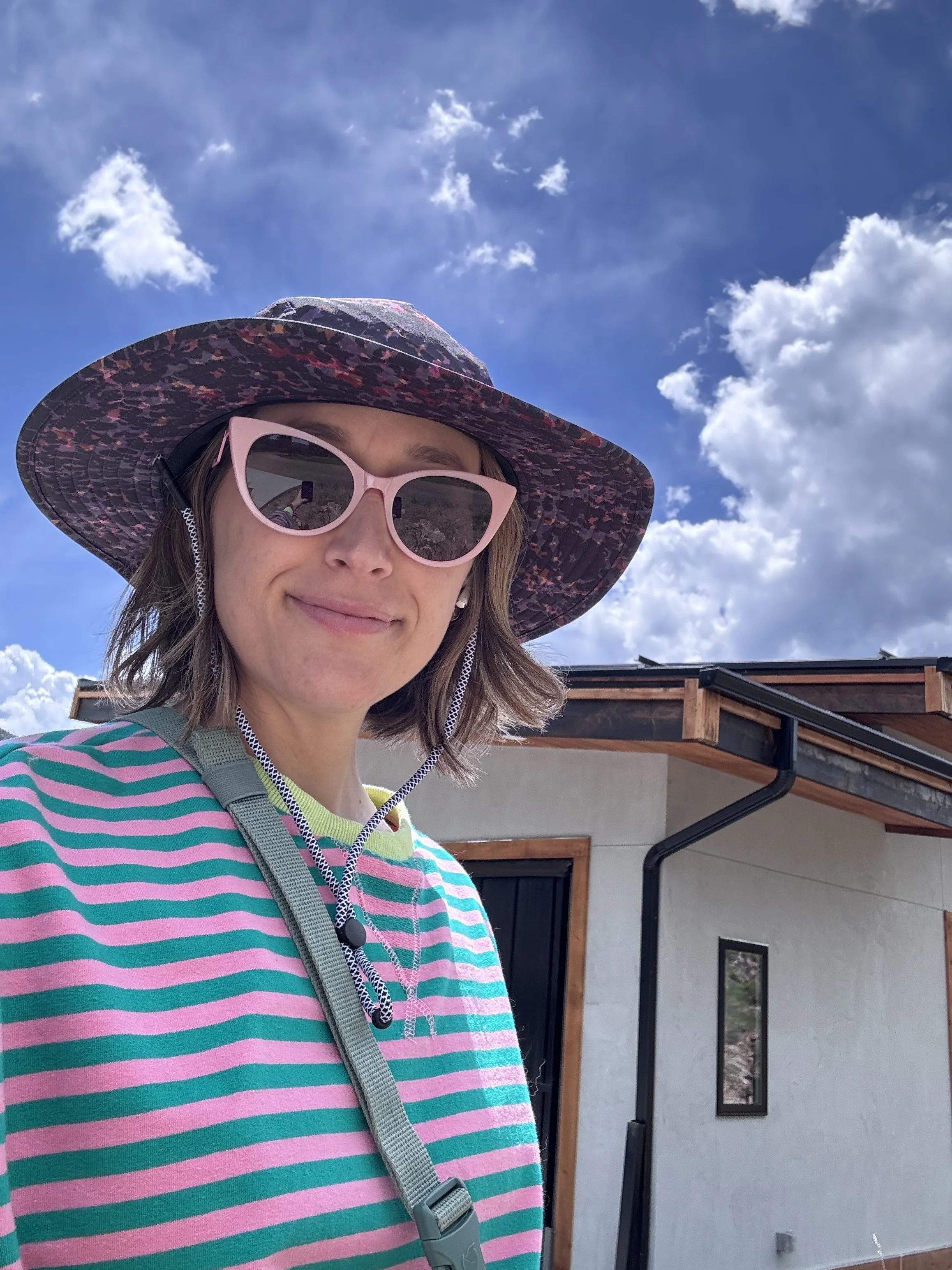Danielle Kosecki wearing sunglasses and a hat outside against a blue sky.