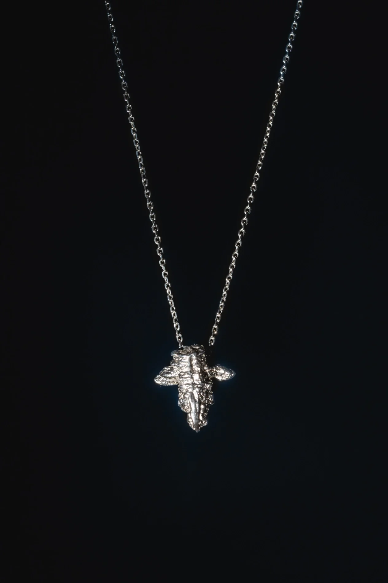 Silver necklace with a pendant shaped like a bee, hanging against a black background.