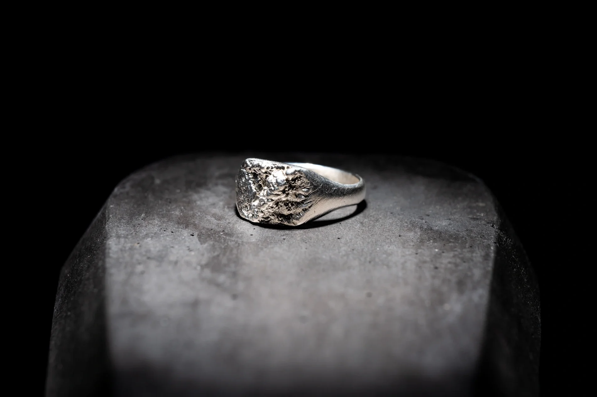Silver ring with a textured, rough surface placed on a gray stone surface against a black background.