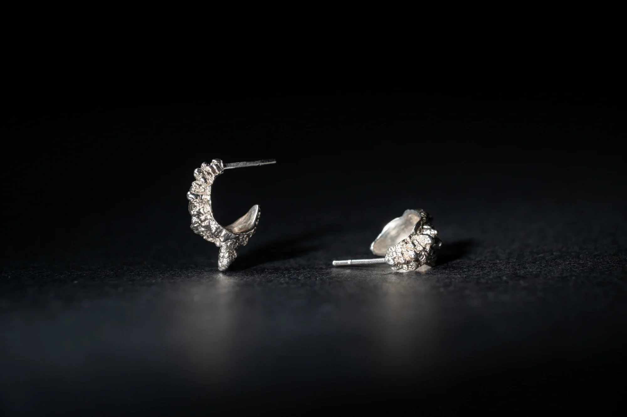A pair of silver crescent-shaped earrings with embedded gemstones on a dark surface against a black background.