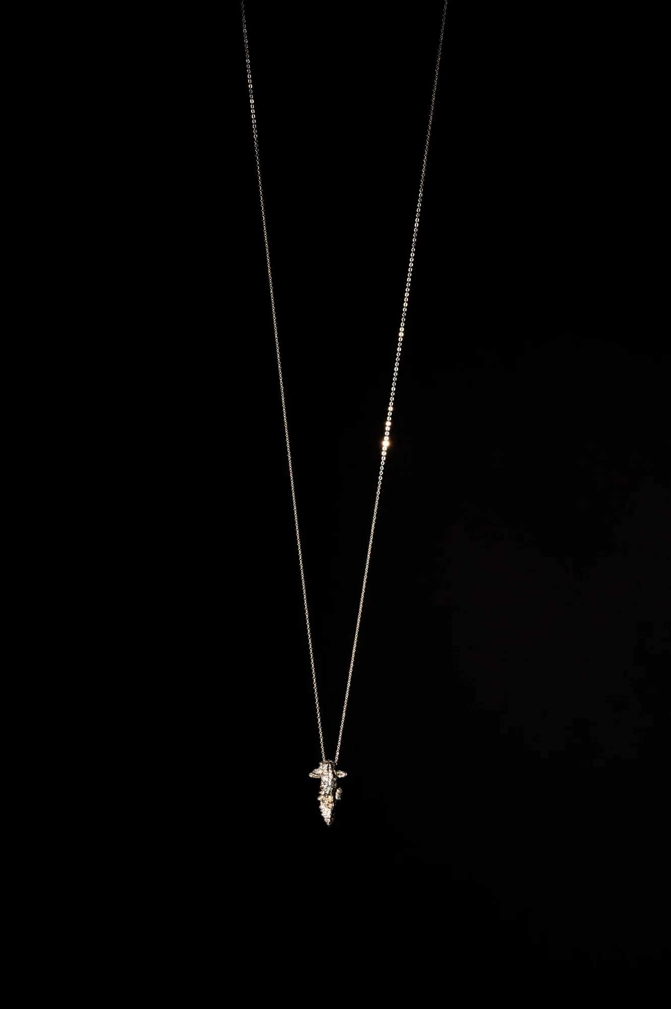 A silver necklace with a pendant featuring a winged figure, displayed against a black background.