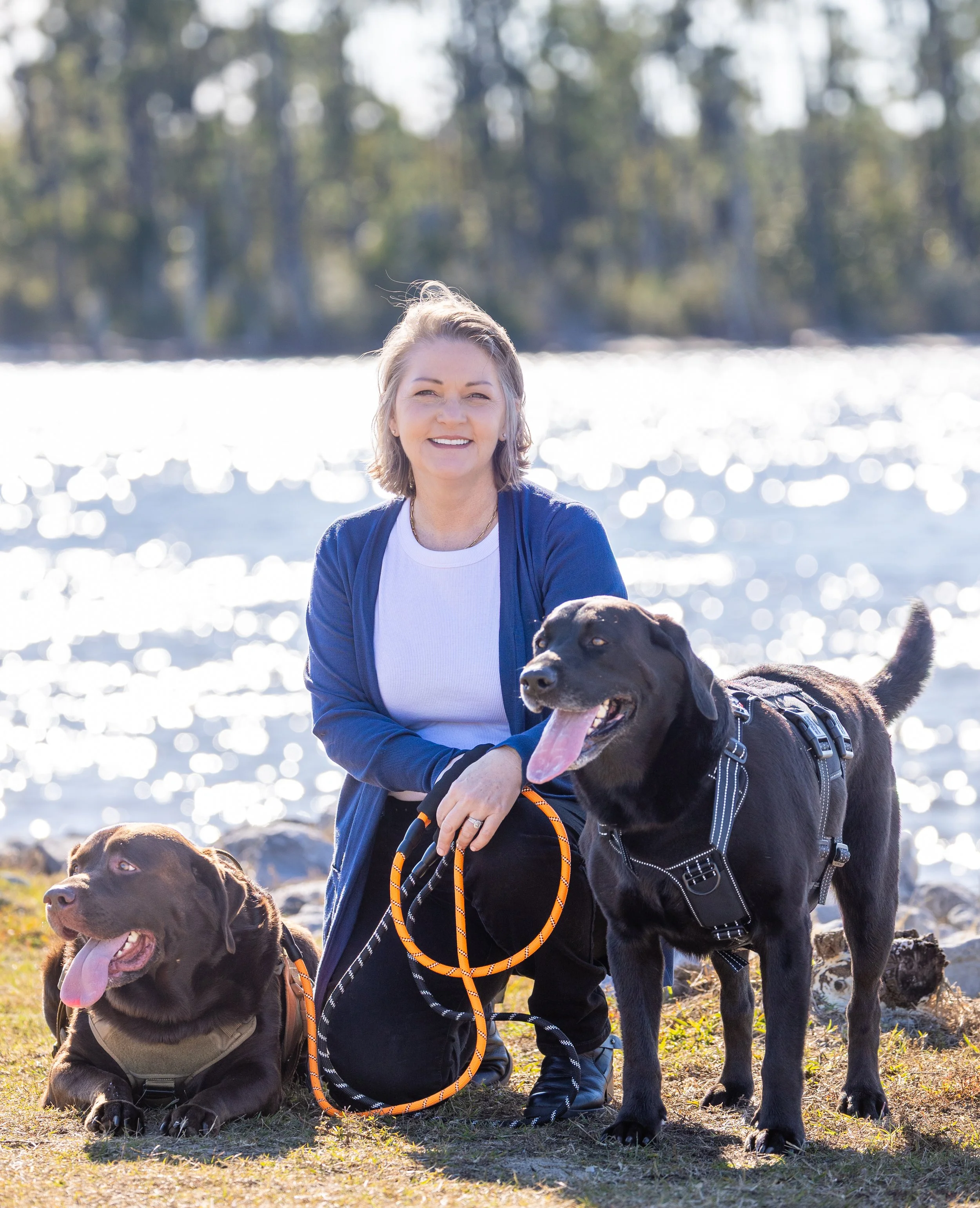 Dr. Angelia Berry smiling with her black lab Buddy and chocolate lab Finn next to the water in Lynn Haven, Florida.