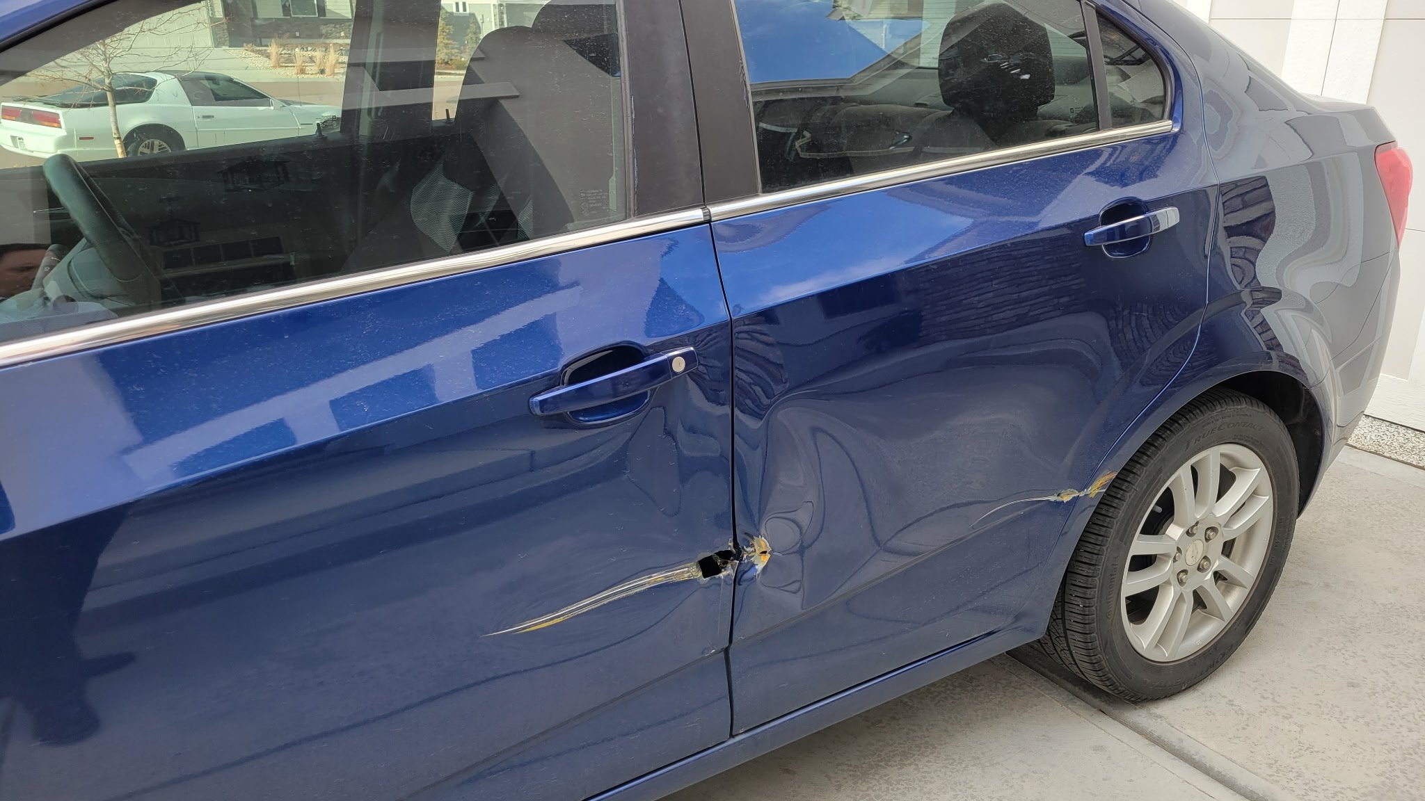 Blue car with damaged front left door, dented and scratched, with the door handle and side mirror visible.