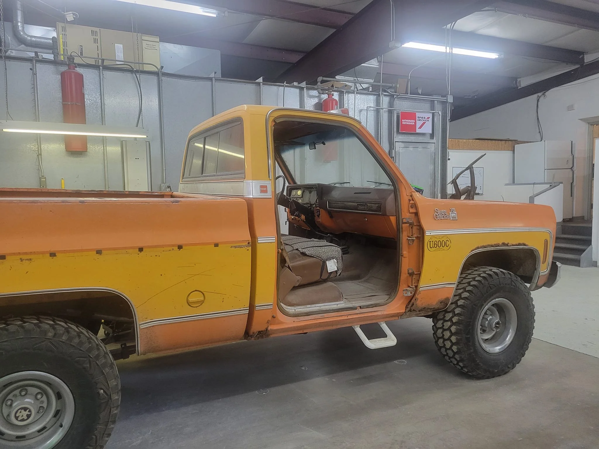 A vintage orange and yellow GMC truck with visible rust and wear, parked indoors in a garage or workshop.