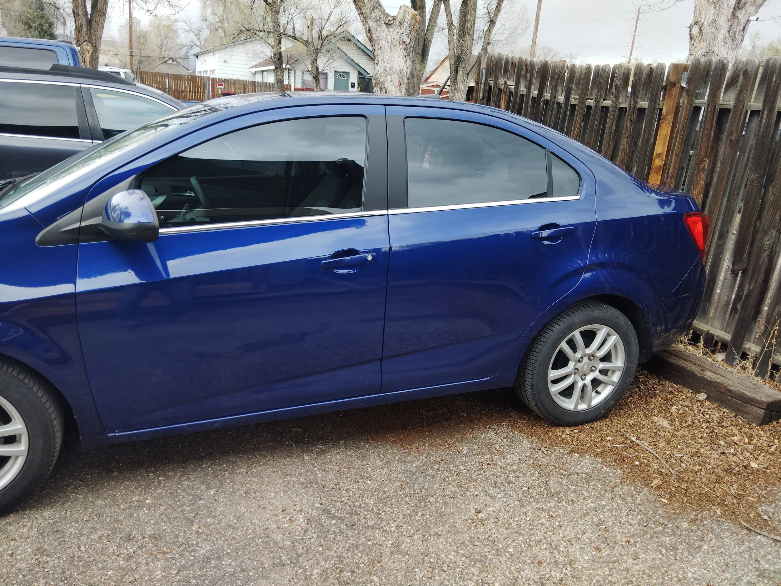 Repaired blue sedan parked on gravel next to a wooden fence.