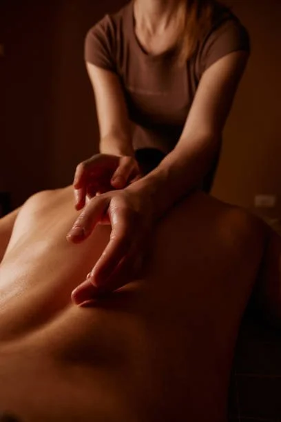 A massage therapist gives a back massage in a dimly lit room.