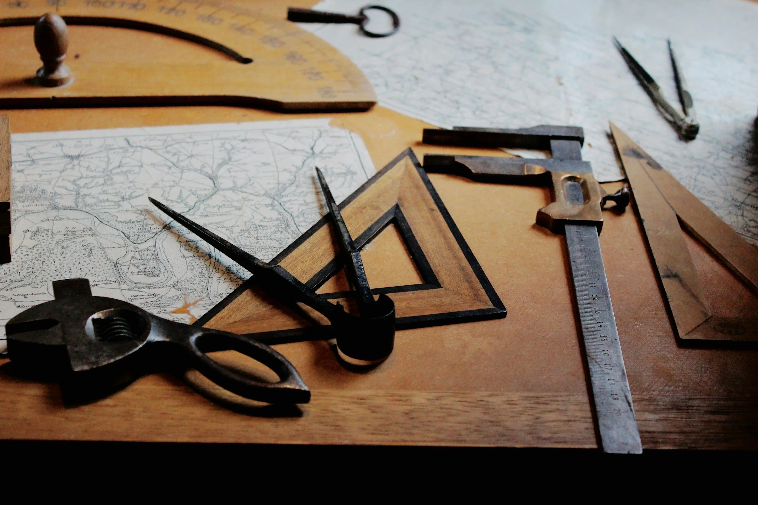 Various drawing tools and a map on a wooden table, including compass, triangle ruler, metal ruler, and brass instruments.