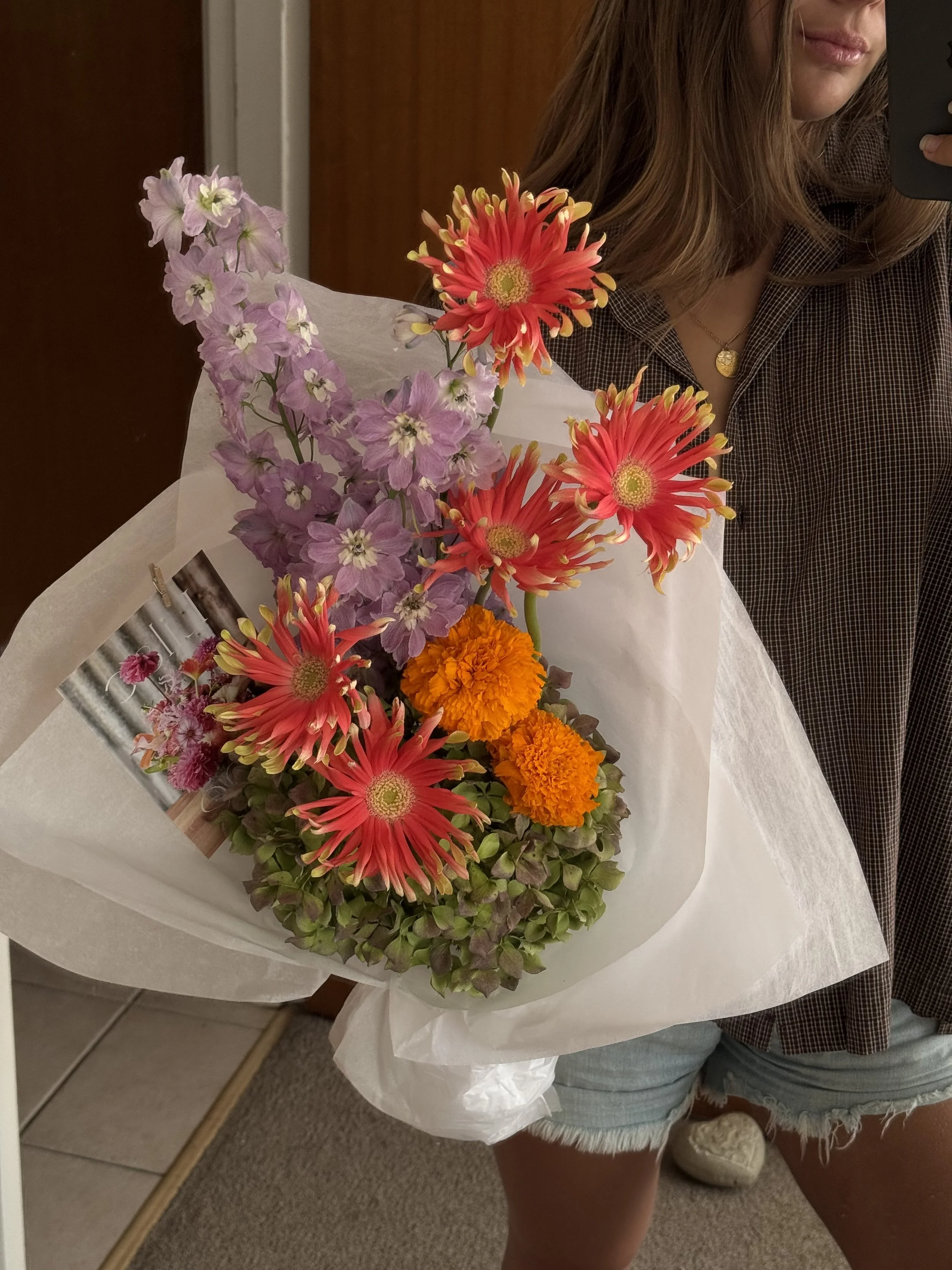Florist holding a fun colourful sculptural bouquet of flowers including pink, orange, and purple flowers