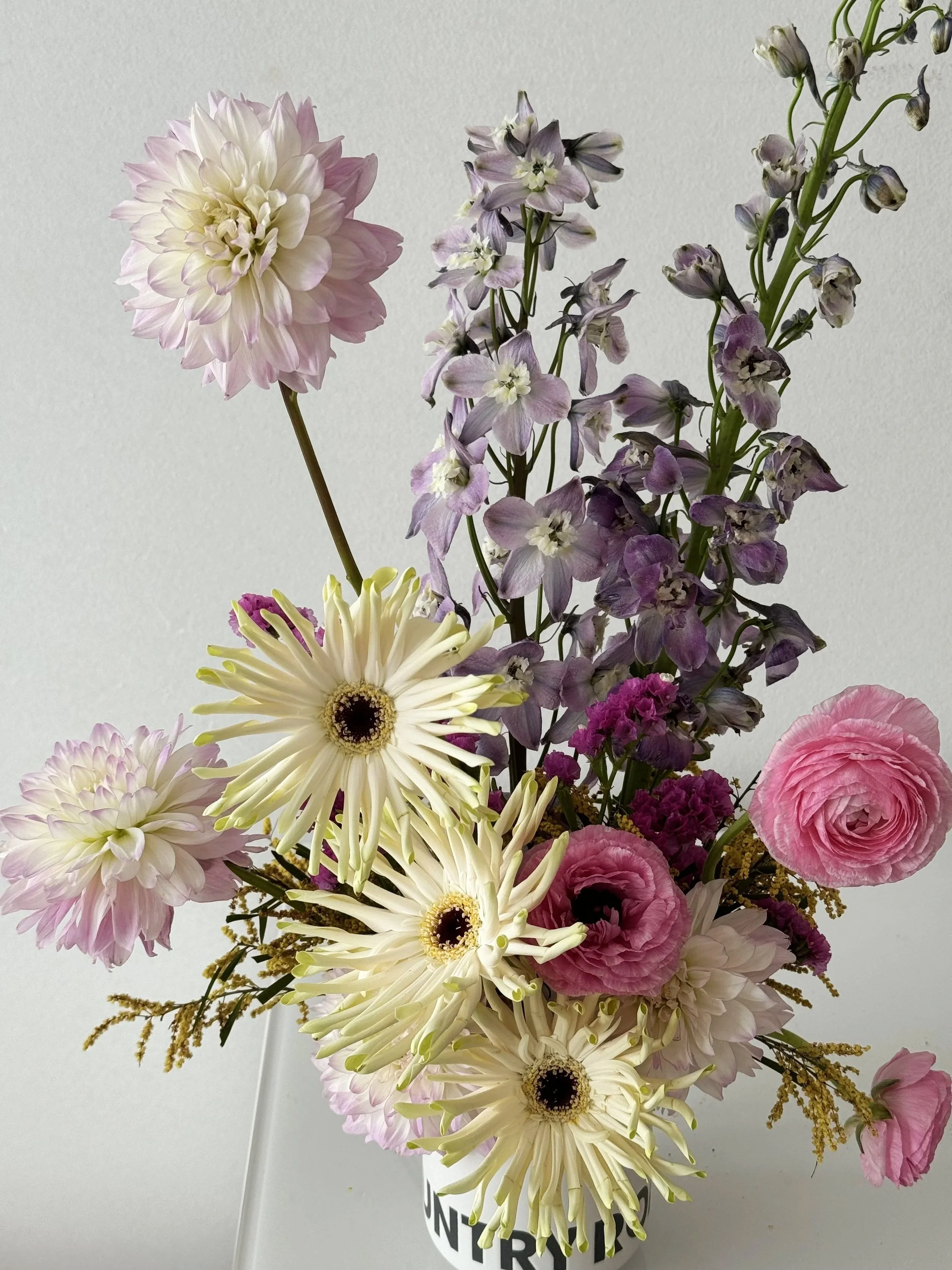 A small floral design of various pink, white, and purple flowers in a white mug.
