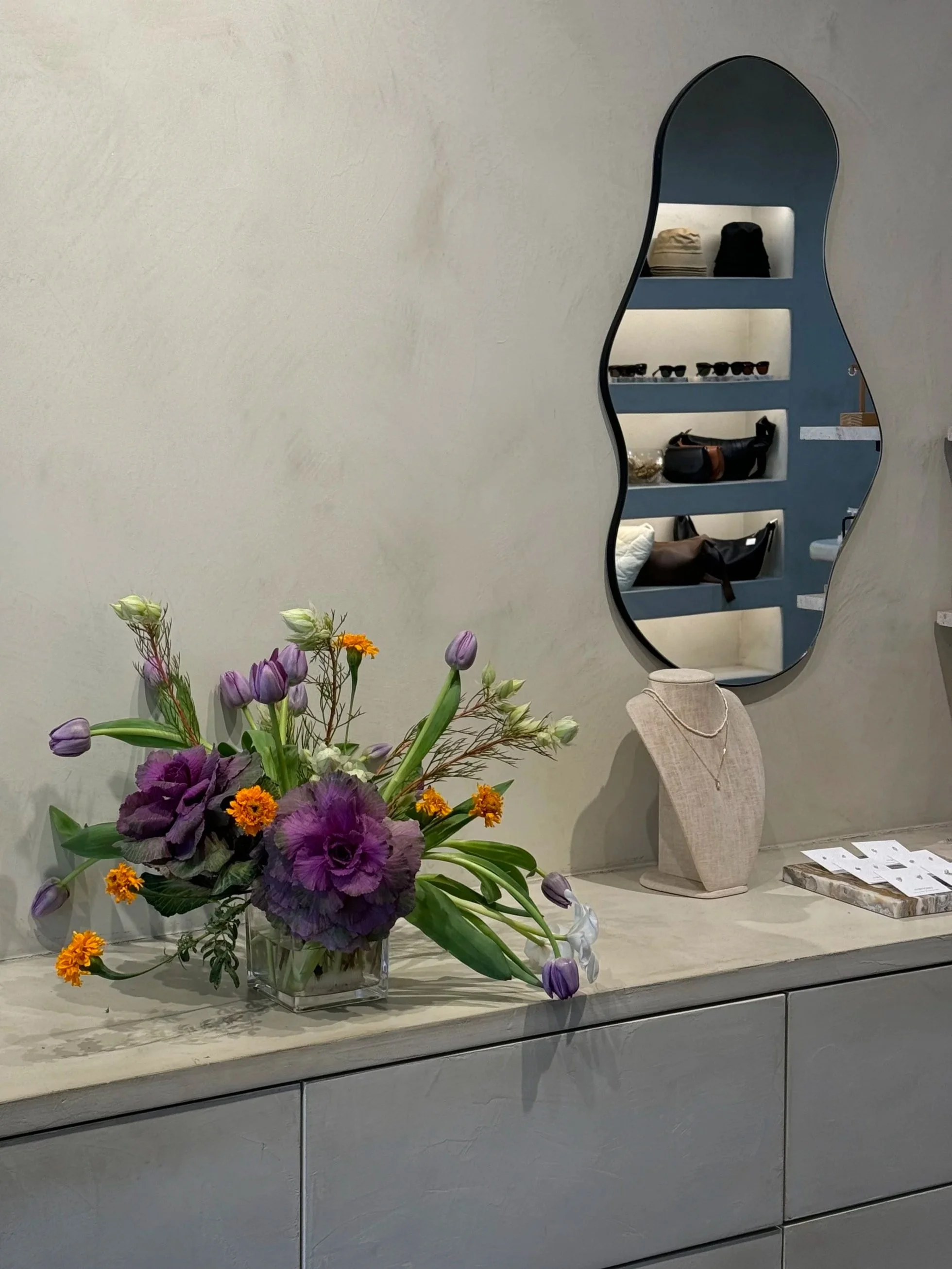 A floral arrangement with purple and orange flowers on a marble countertop, in front of a display of jewellery inside a jewellery store