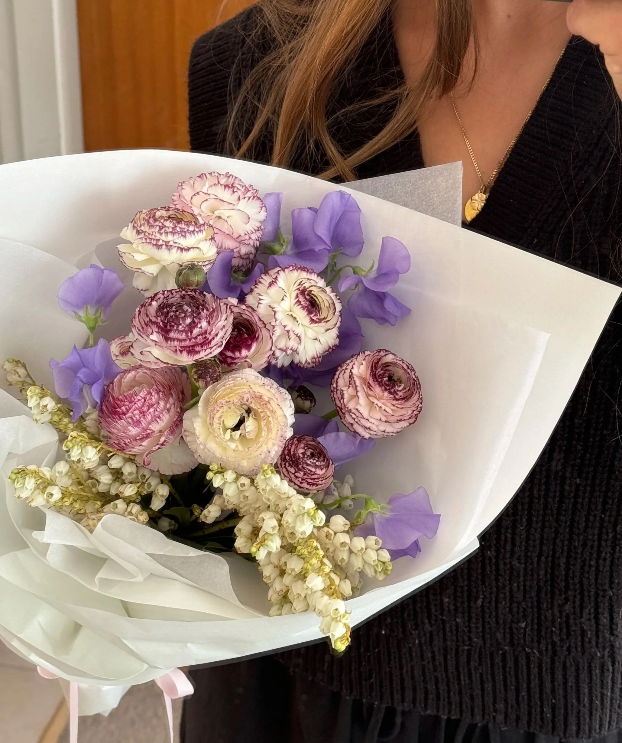 Florist holding a bouquet of purple and pink flowers wrapped in white paper.