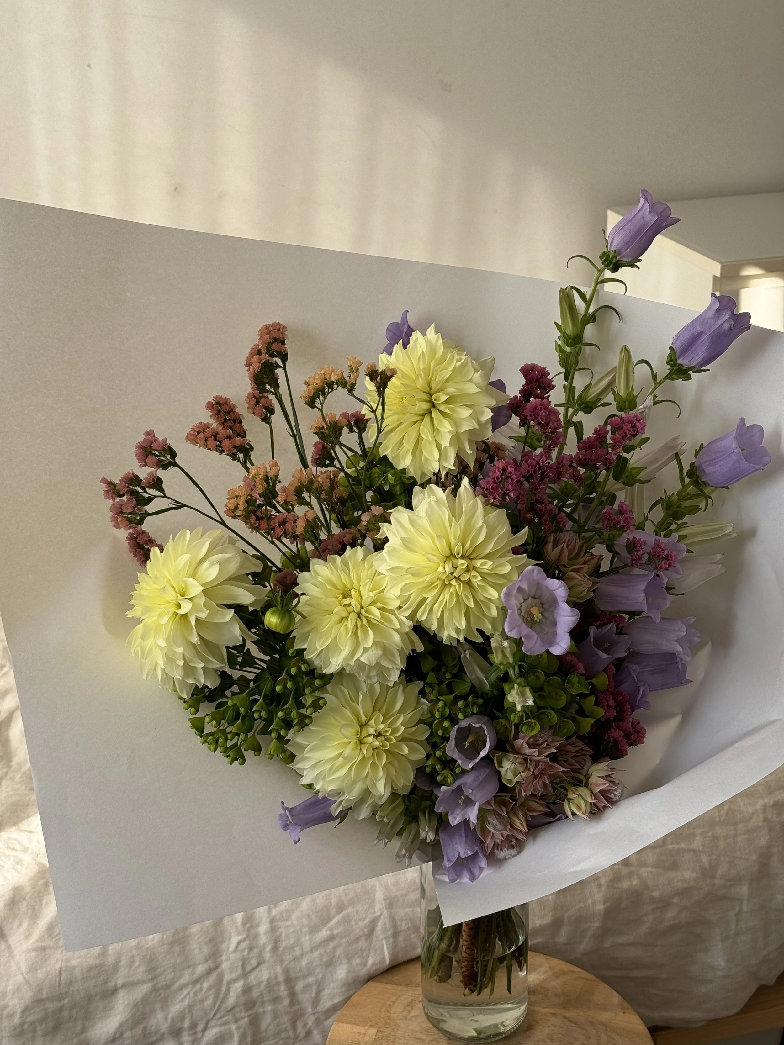 A bouquet of yellow dahlias, purple bellflowers, pink statice, and other mixed flowers in a glass vase.