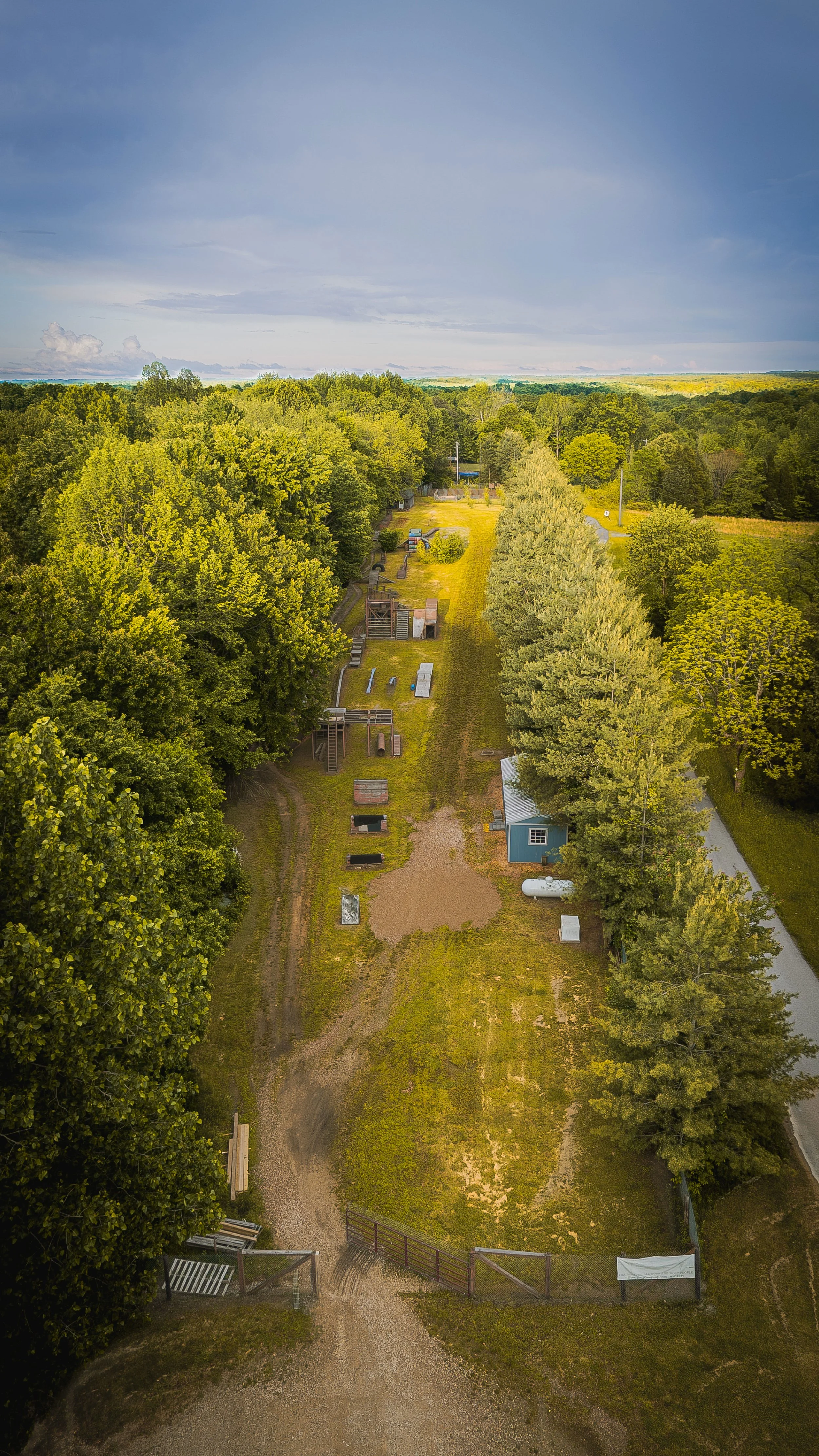 An aerial view of a yard with trees, a gravel path, small structures, and playground equipment.