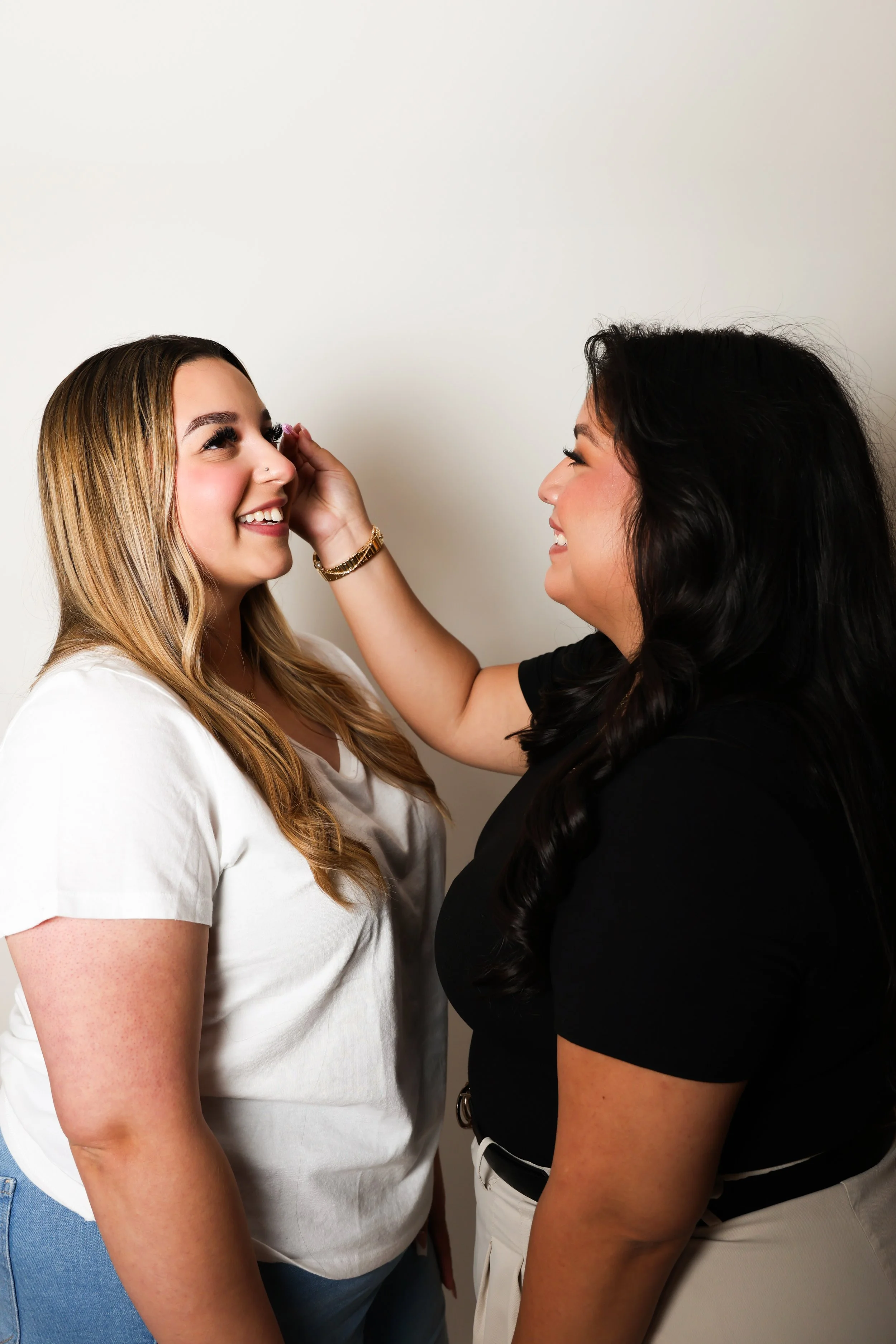 Two women smiling at each other, one touching the other's face in a friendly gesture.