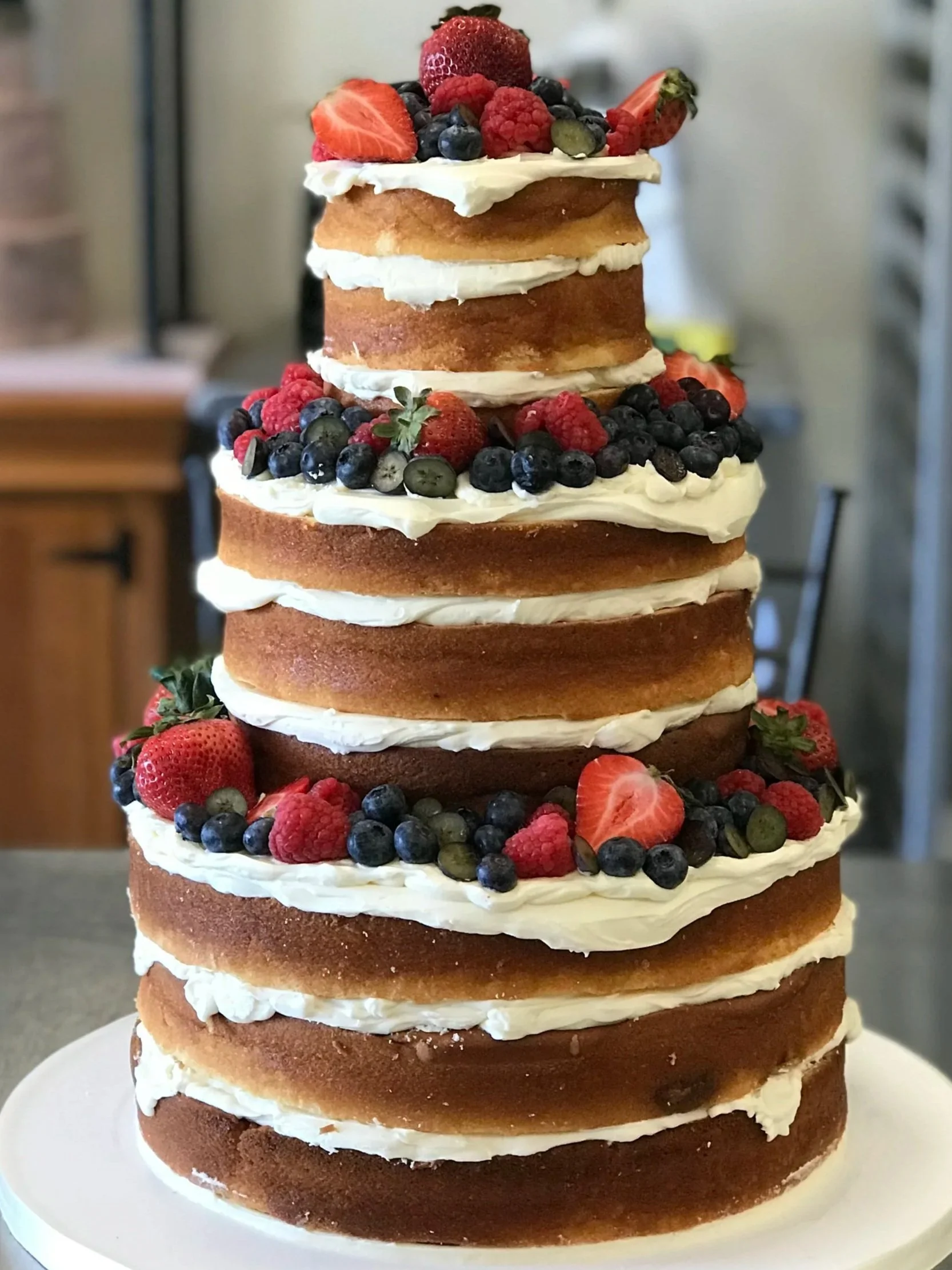 Layered cake with multiple layers of vanilla sponge, cream cheese frosting, and fresh berries including strawberries, raspberries, blueberries, and blackberries.