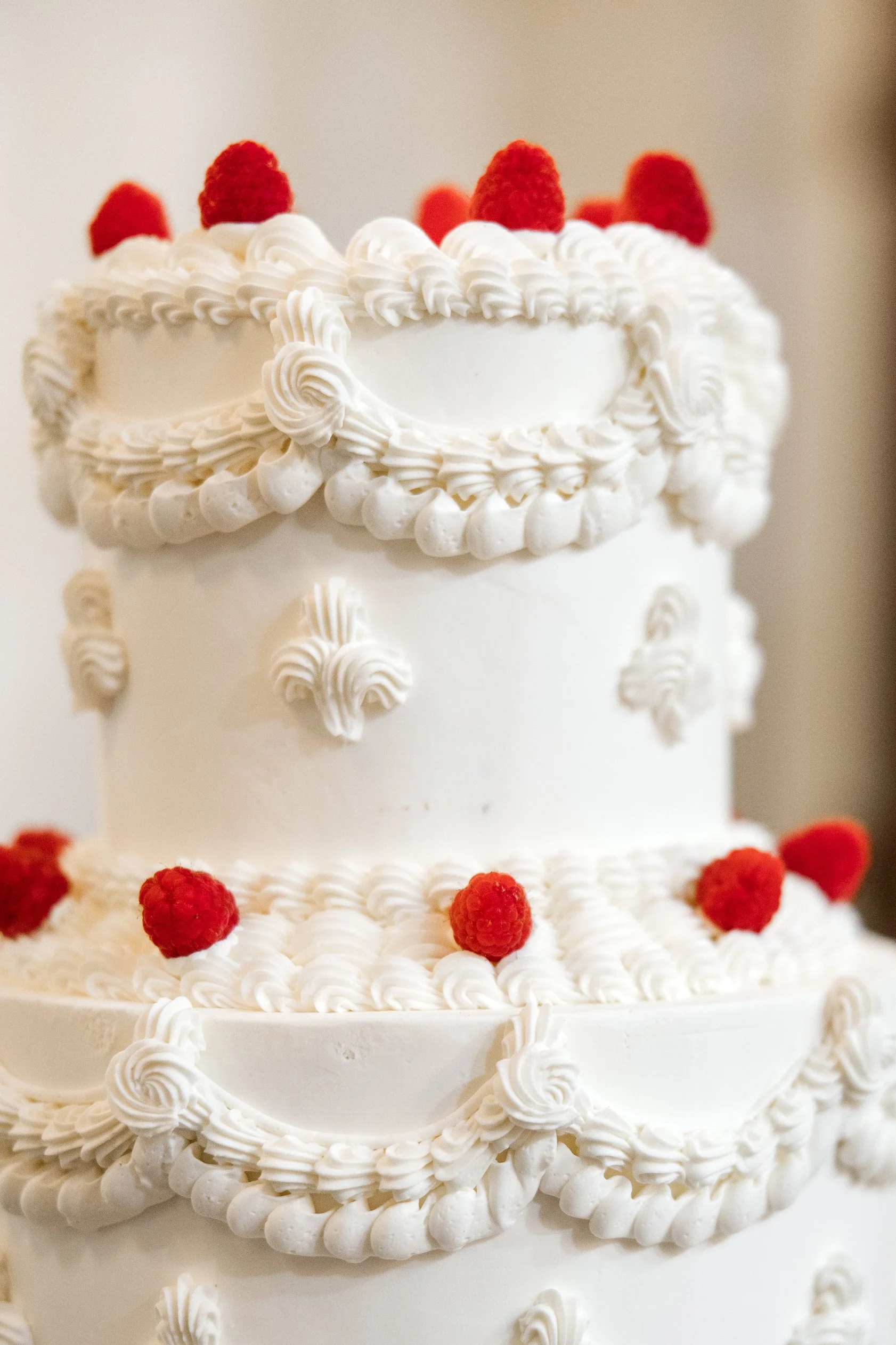Close-up of a white, multi-tiered cake decorated with white icing and fresh raspberries on top and around the base.