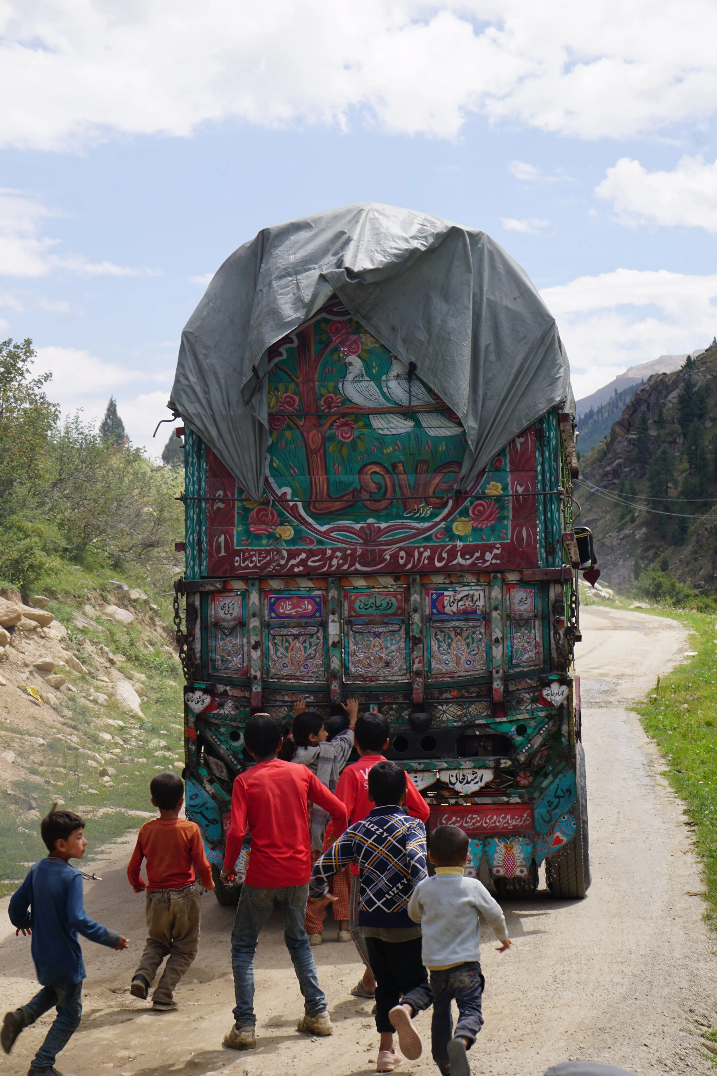 Children playing near a colorful, decorated truck on a mountain road.