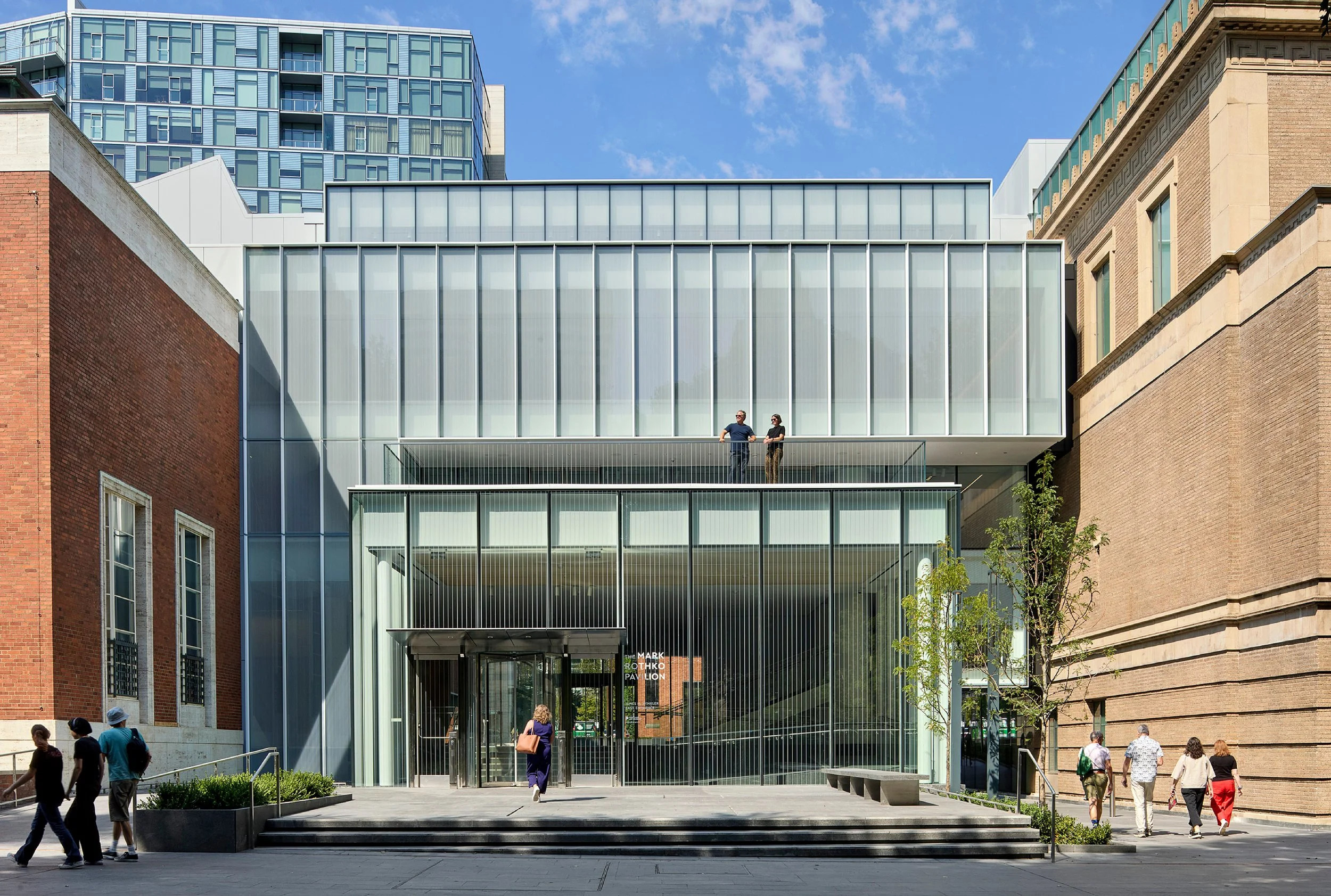 Modern building with large glass windows and yellow lighting interior, seen during evening or night.