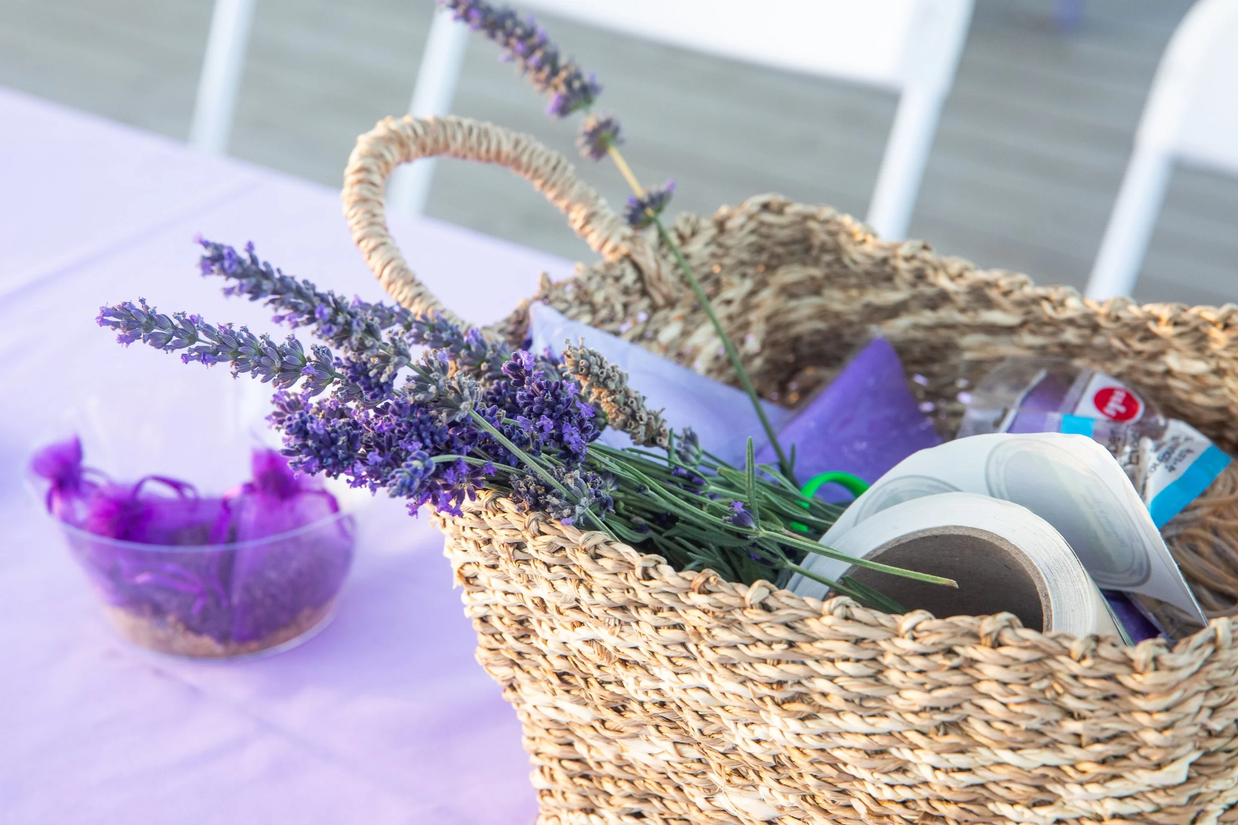 A basket filled with purple and lavender flowers sitting on a table with lavender flowers in a purple container nearby.