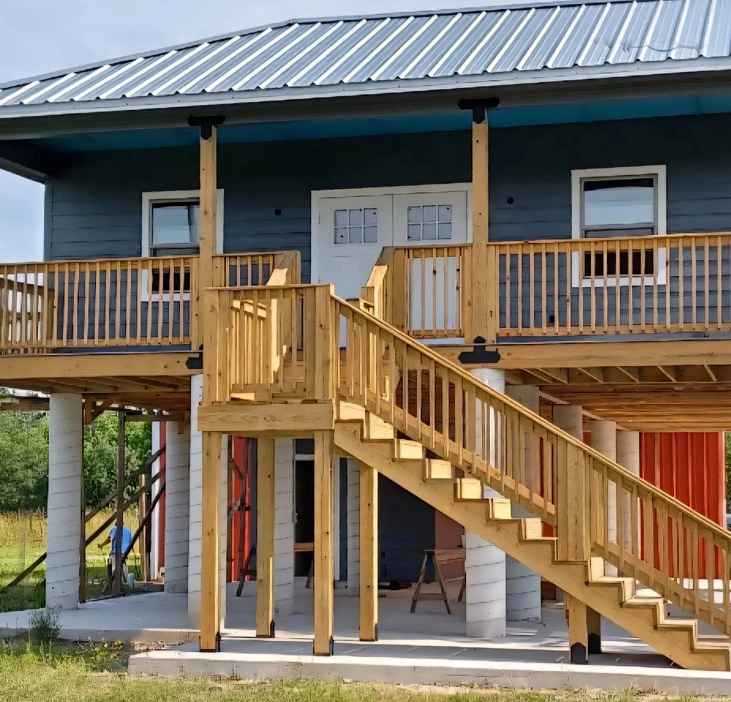 Wooden staircase and railing leading up to the porch of a blue house under construction.