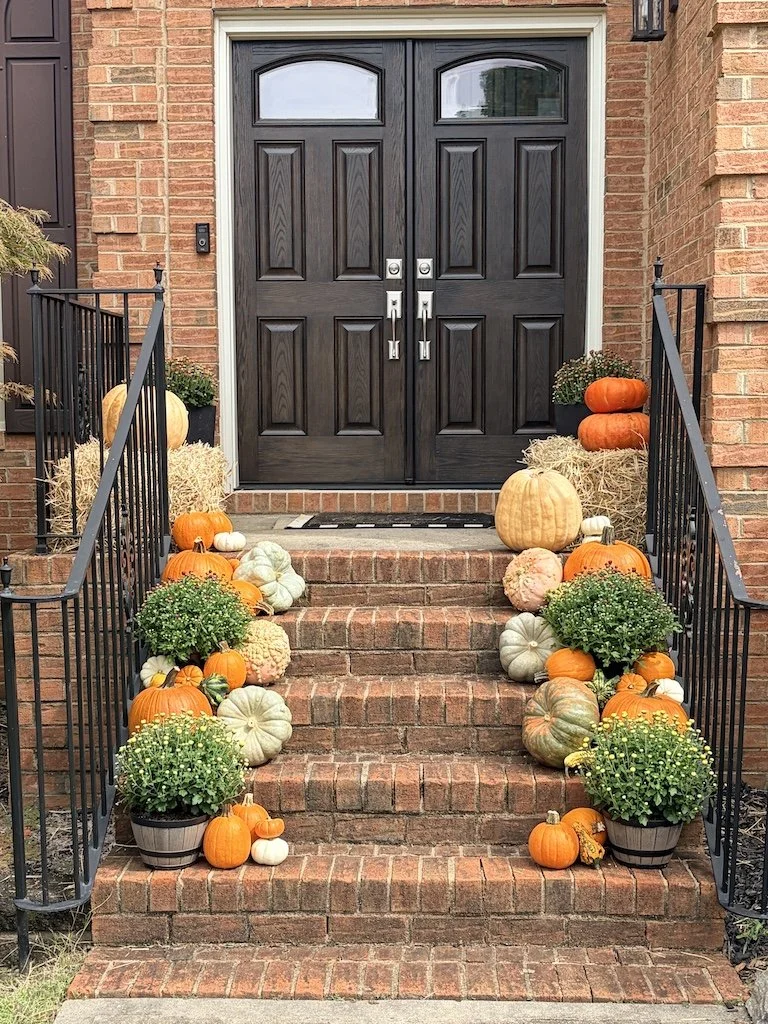 Decorated front porch stairs with pumpkins, gourds, hay bales, and potted mums for fall or Halloween.