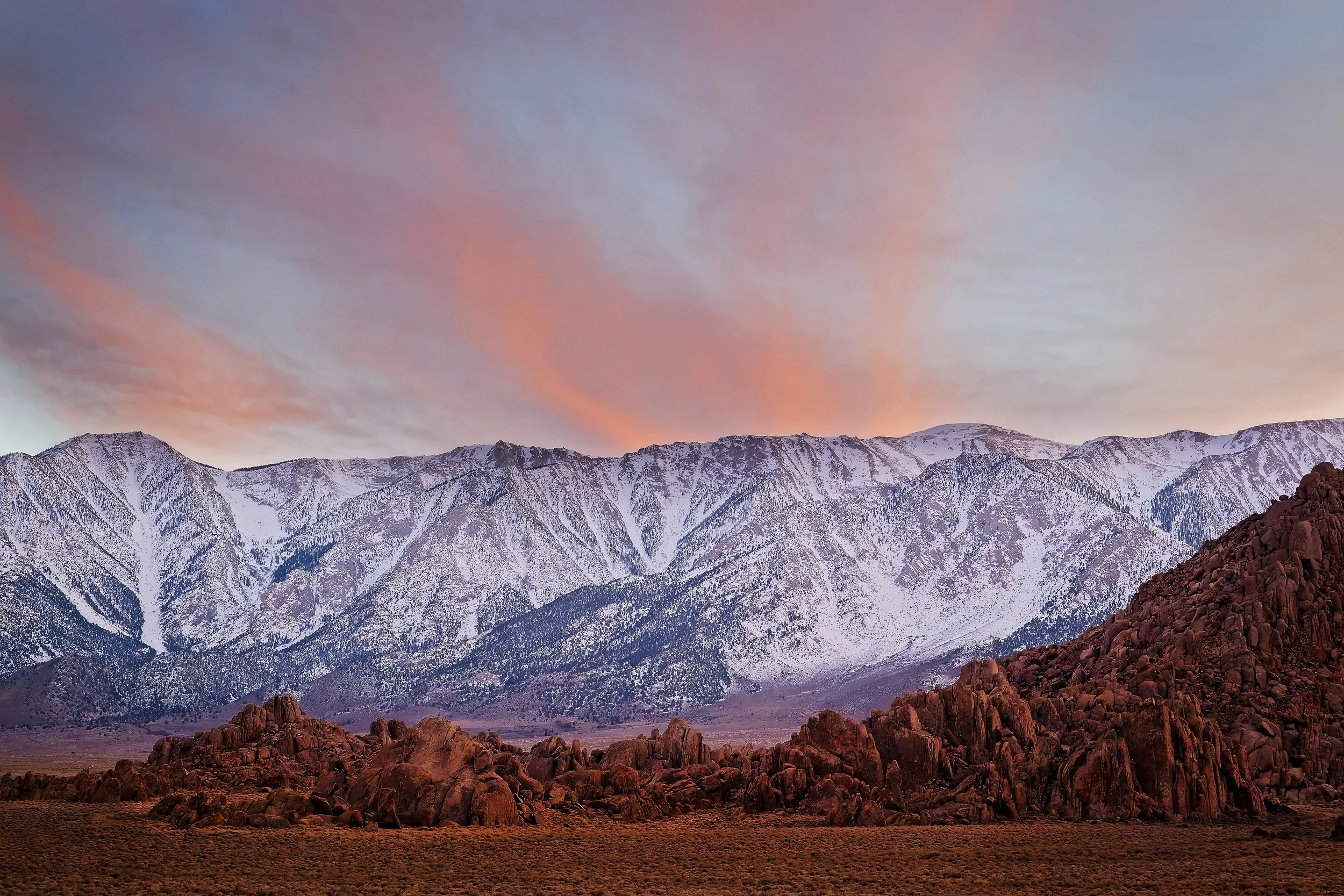 Snow-capped mountains with rocky foreground and colorful sunset sky.