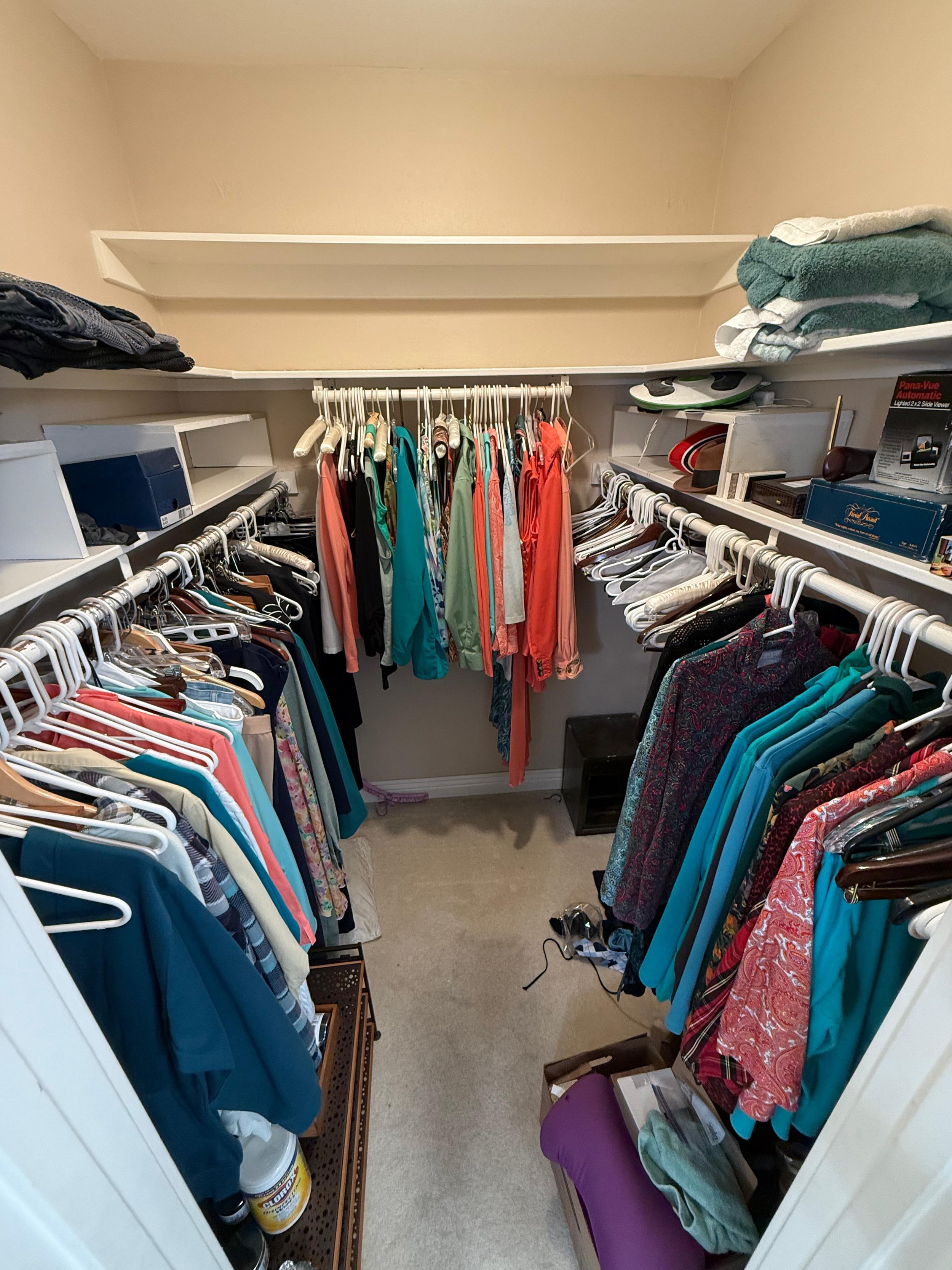 A walk-in closet with clothing on racks, folded towels on shelves, and various boxes and containers.