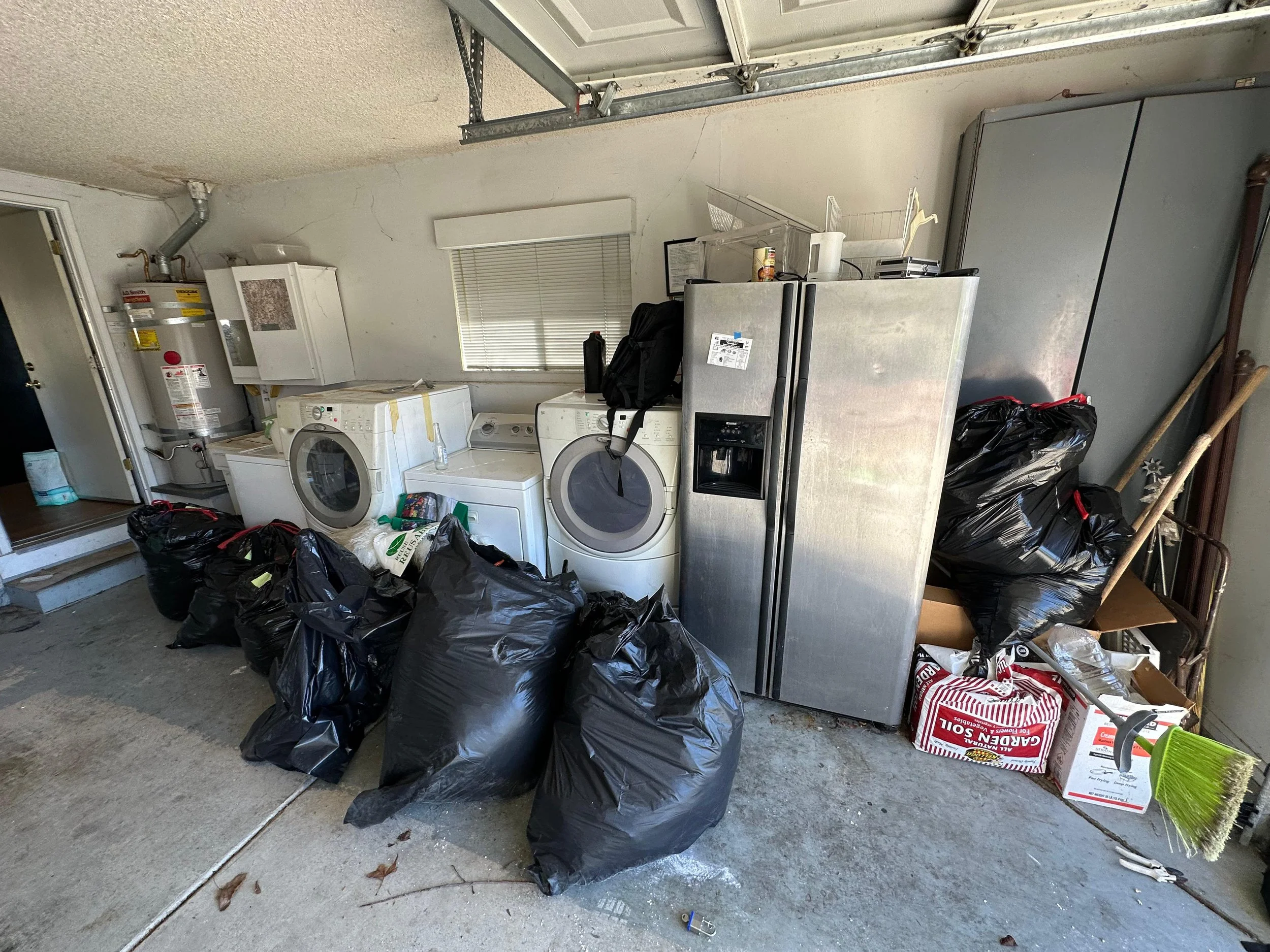 Garage with washing machine, dryer, refrigerator, cleaning supplies, and trash bags