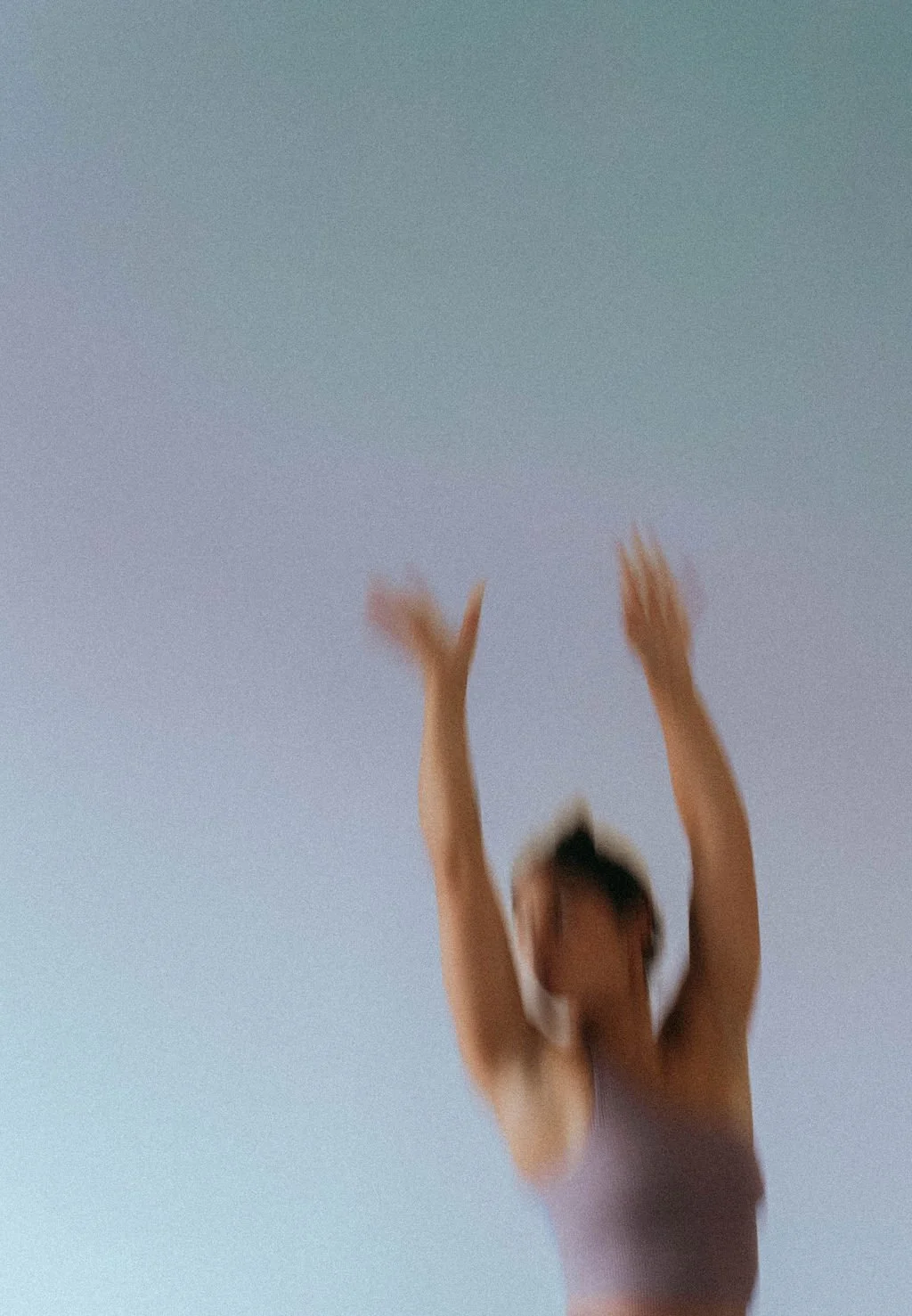 Blurred image of a woman reaching upward with both arms extended, standing against a gradient sky background.