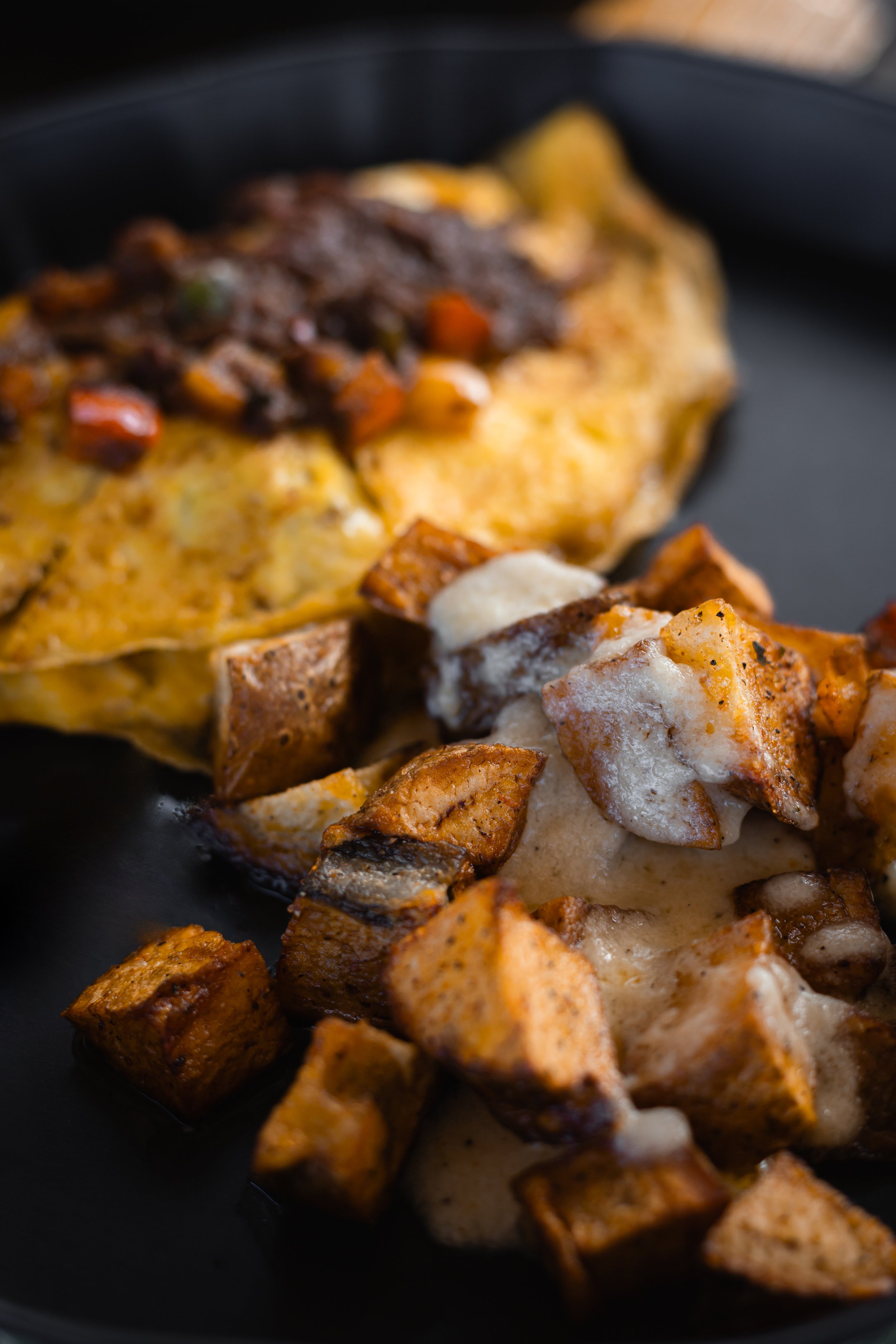 A plate with roasted potatoes topped with melted cheese, crispy edges, and seasoning, alongside a cheese omelette topped with cooked vegetables.