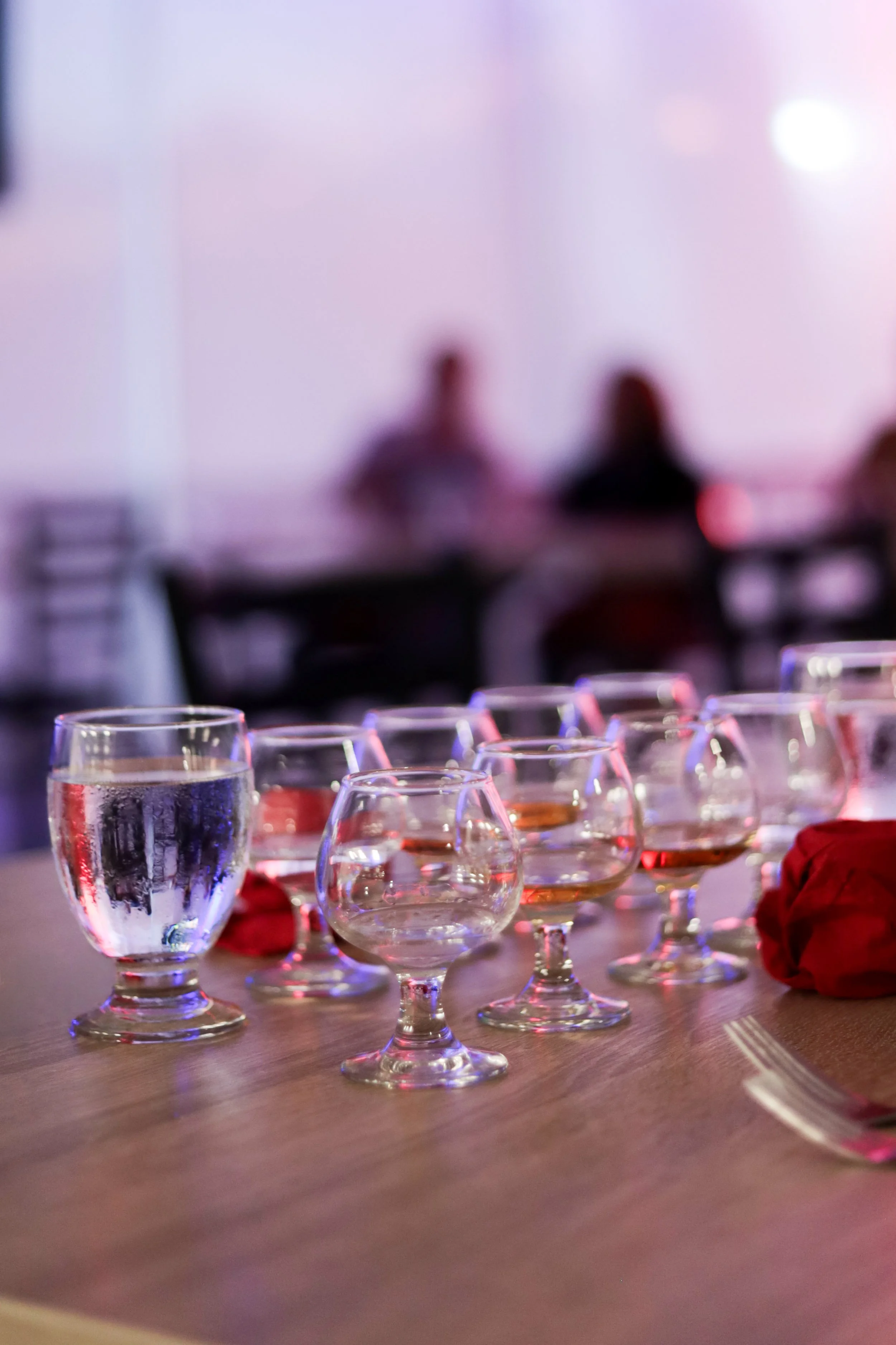 Multiple glasses of water and pink wine on a table with blurred people in the background.