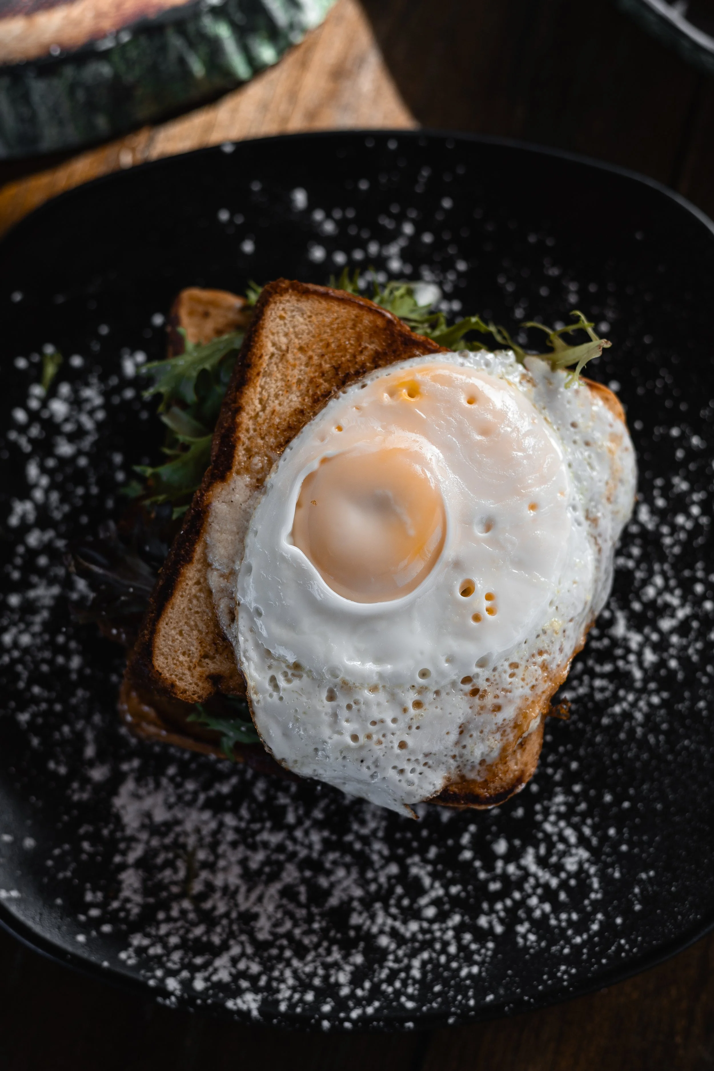 Fried egg on toasted bread with greens on a black plate.