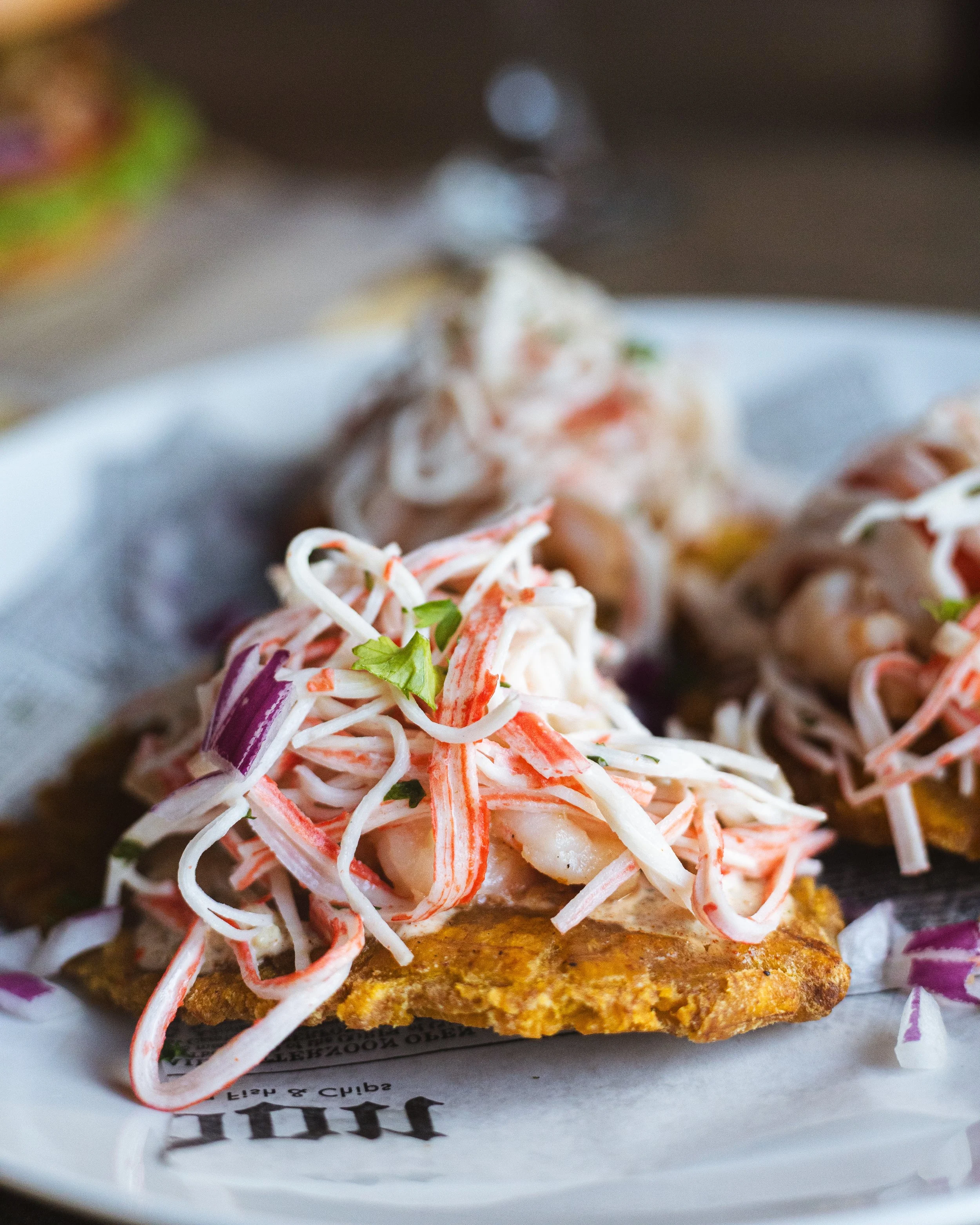 Close-up of a fish taco topped with shredded cabbage and garnished with chopped herbs on a white plate.