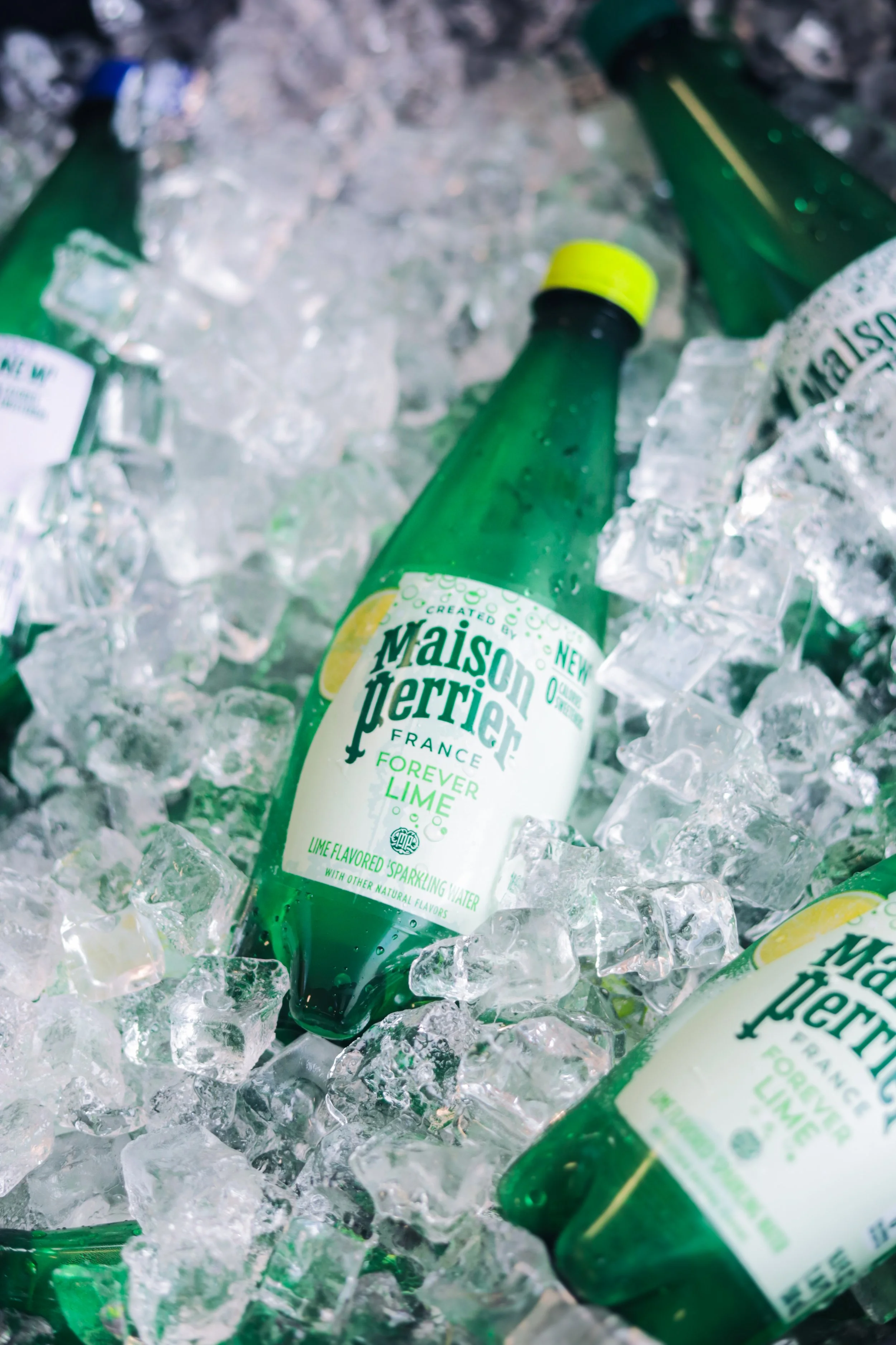 Green bottles of Maison Perrier sparkling water with lemon flavor resting on ice.