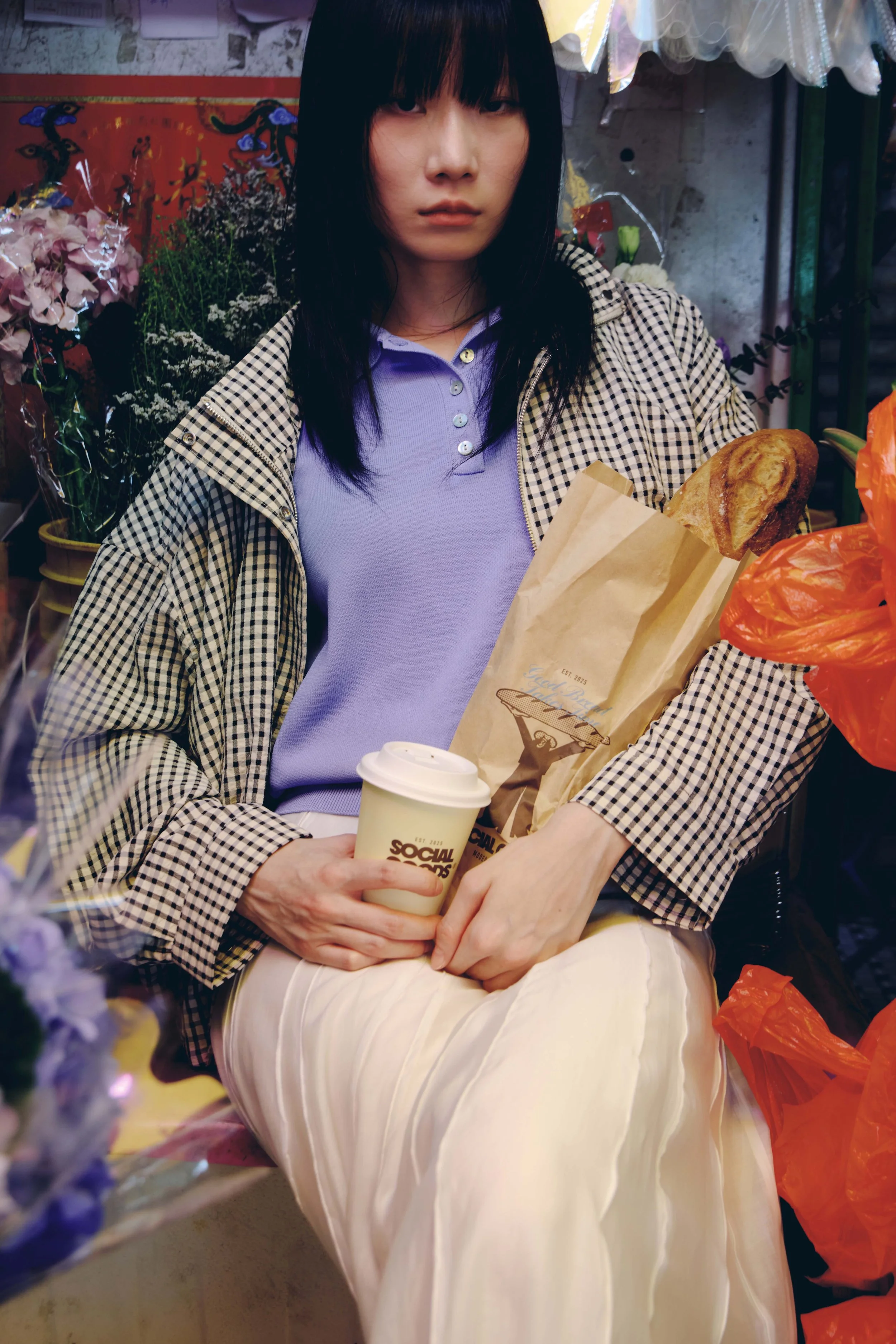 A young woman in a Hong Kong flower shop holds a paper bag and iced drink from Social Goods, surrounded by fresh flowers.