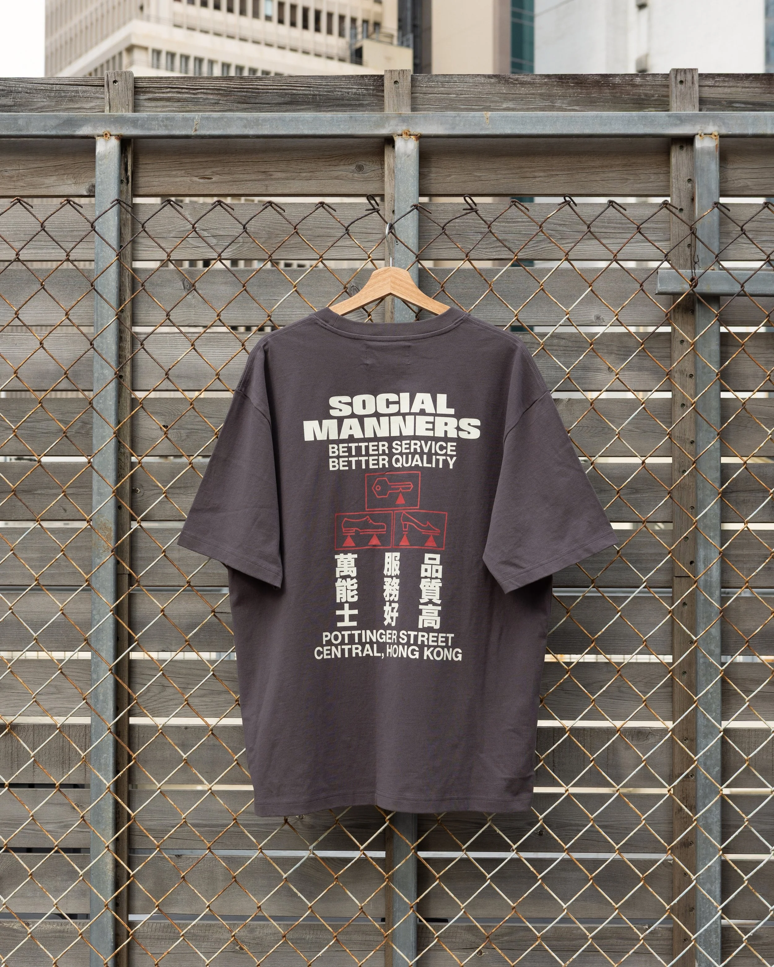 Social Manners black T-shirt by Social Goods, hanging against a Hong Kong cityscape.