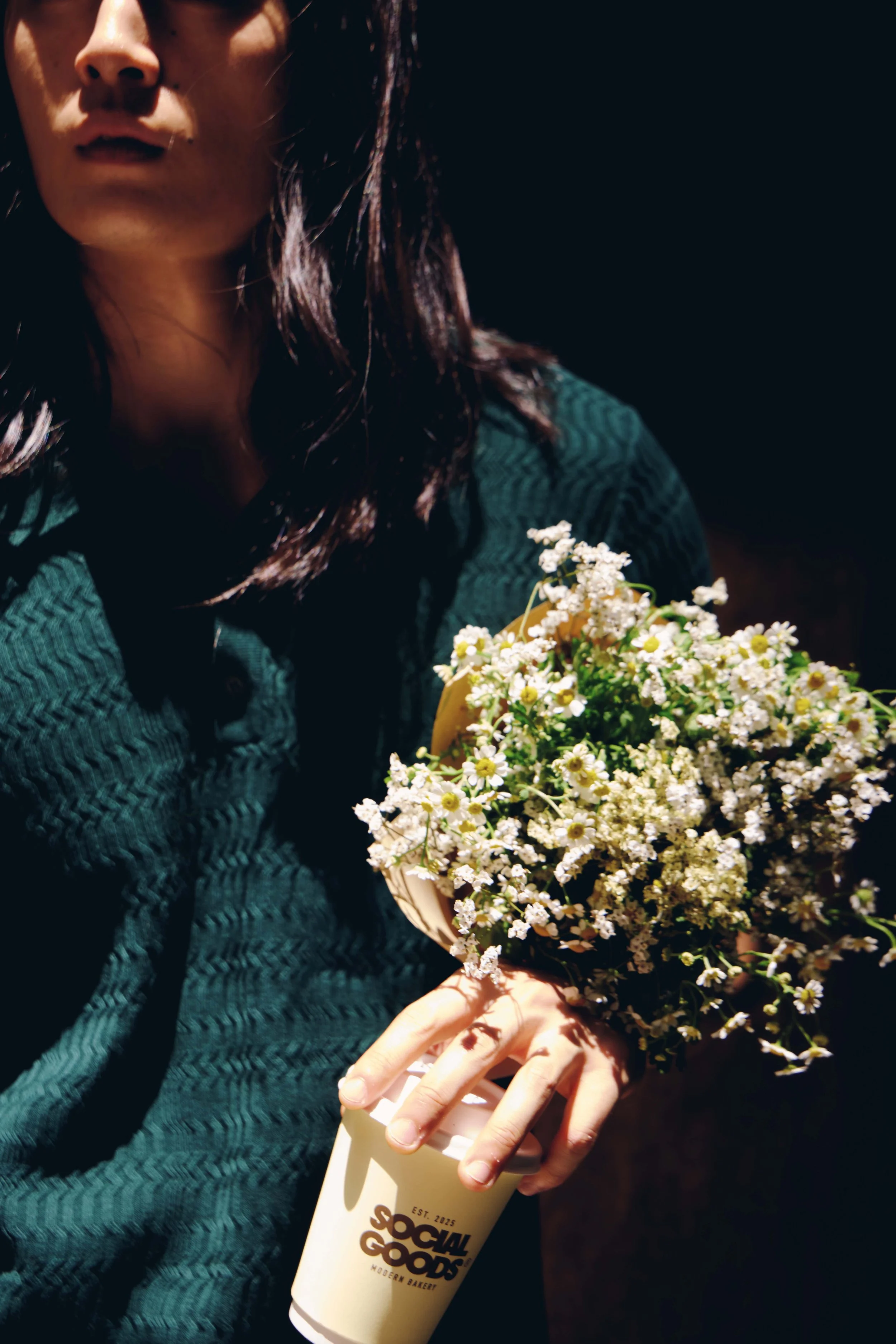 A woman holds a bouquet of white daisies alongside a Social Goods coffee cup, pairing the neighbourhood florist with the bakery's modern edge.