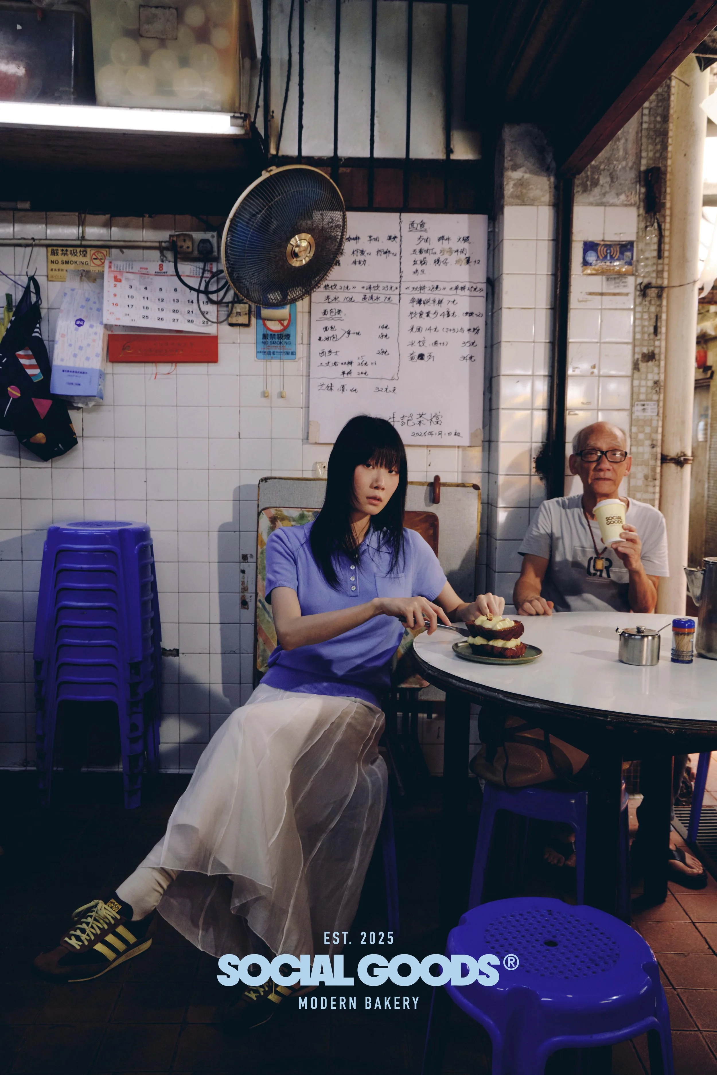 Two customers share pastries and coffee at a table inside the Social Goods bakery, its tiled walls and handwritten signs in view.